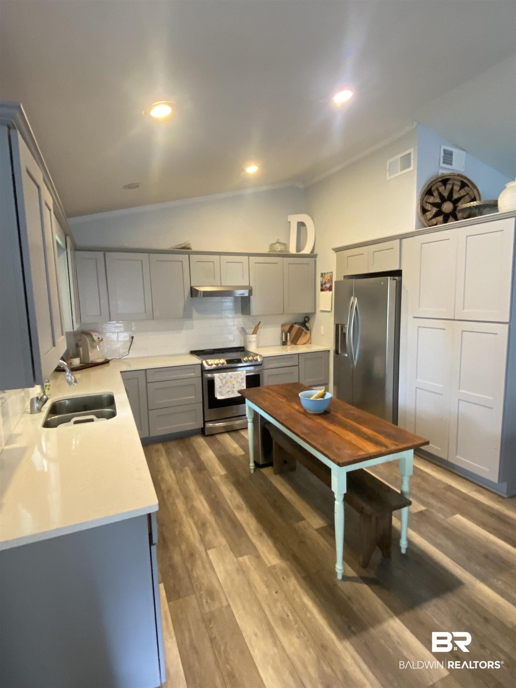 Image 4: Kitchen featuring a stainless steel appliance suite, wood-finish flooring, two-tone cabinetry with gray base cabinets and light upper cabinets, recessed lighting, and a vaulted ceiling