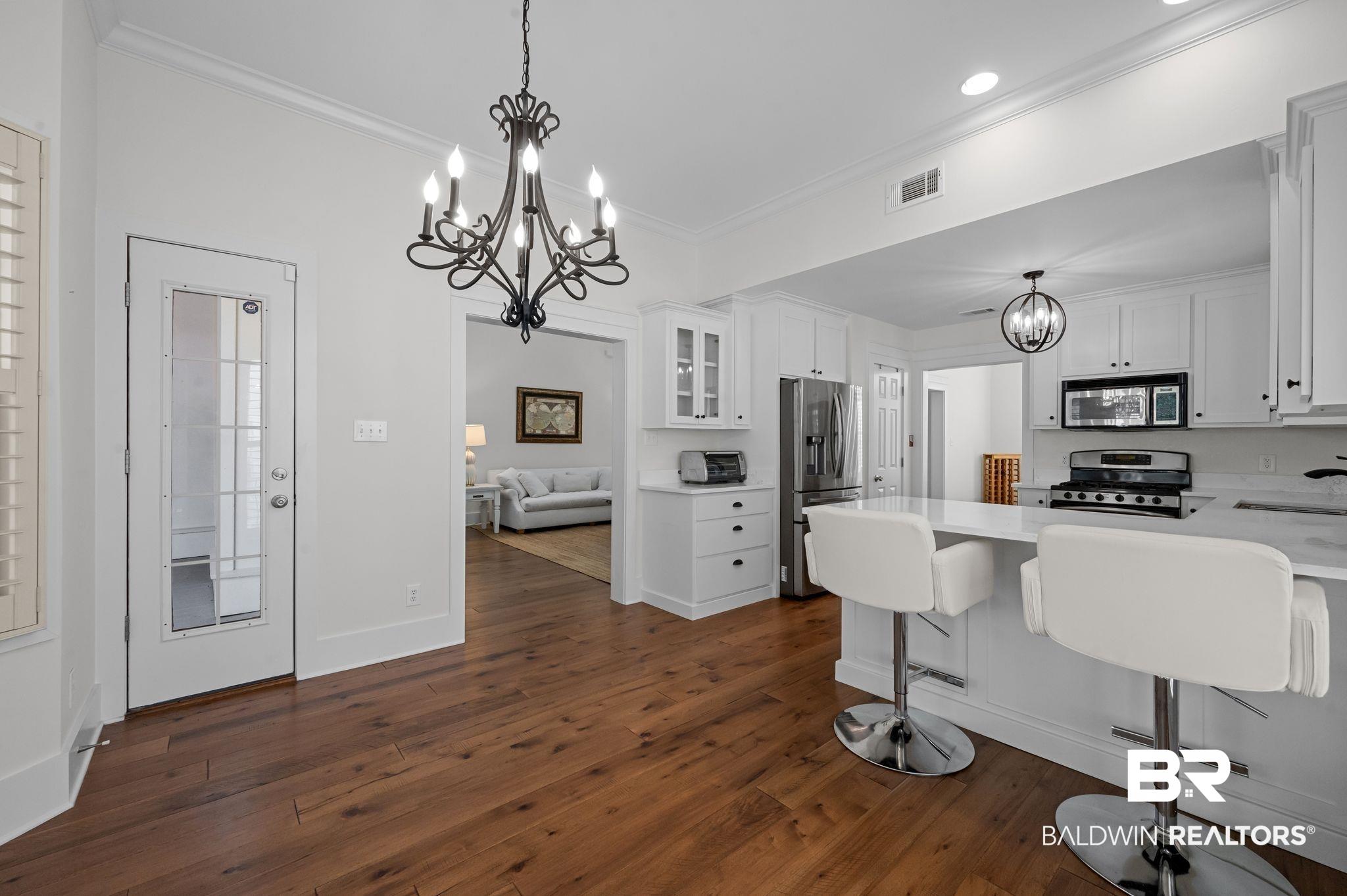 Image 4: Kitchen featuring a chandelier, white cabinets, a kitchen bar, crown molding, and dark wood-type flooring