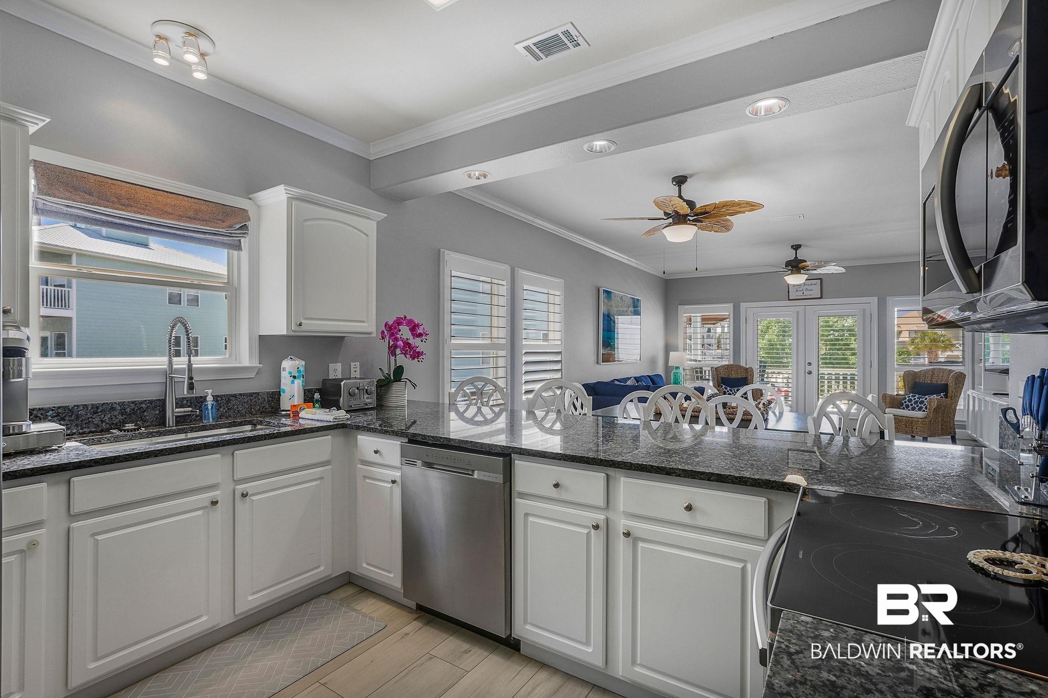 Image 2: Open-concept kitchen featuring white cabinetry, dark stone countertops, stainless steel appliances, a built-in electric cooktop, and wood-finish flooring