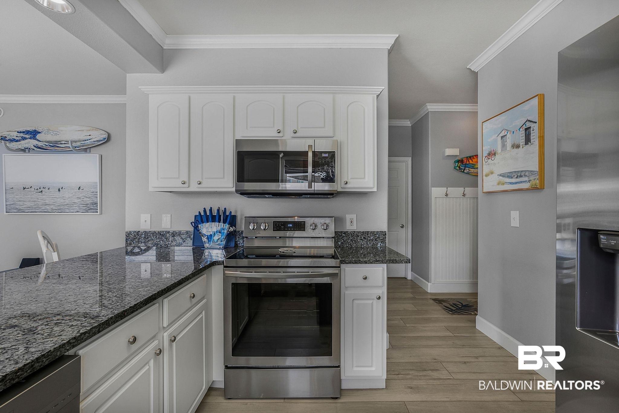 Image 3: Kitchen featuring granite countertops, white cabinetry, and stainless steel appliances