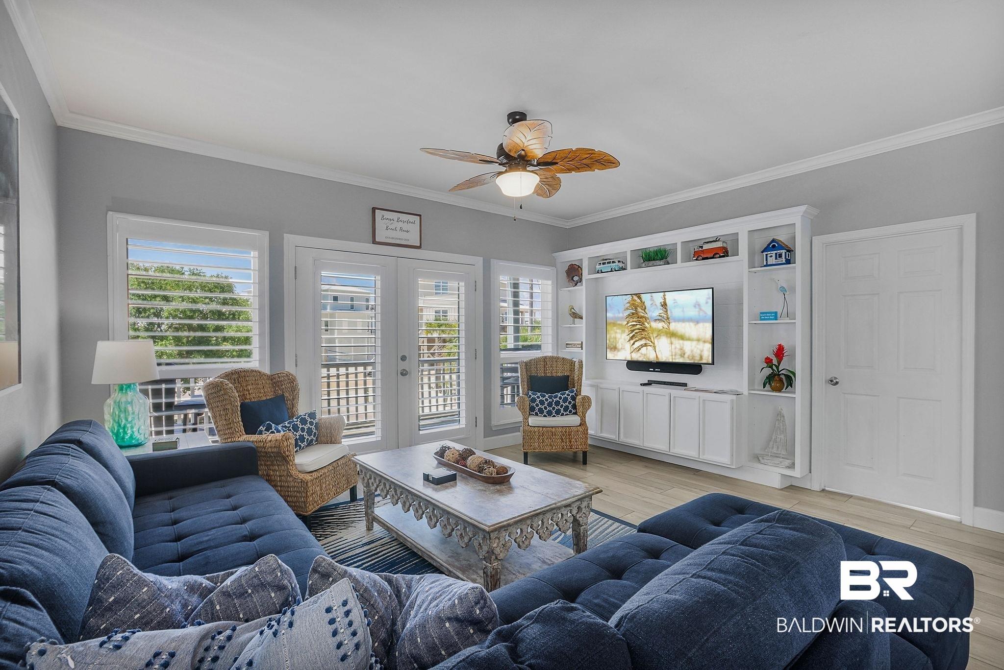 Image 4: Living area featuring light wood-finish flooring, a ceiling fan, and a built-in entertainment center with shelving and lower cabinetry