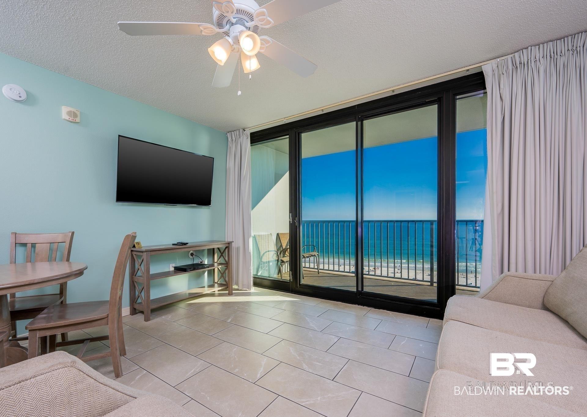 Image 4: Tiled living room with a wall of windows, ceiling fan, and a textured ceiling
