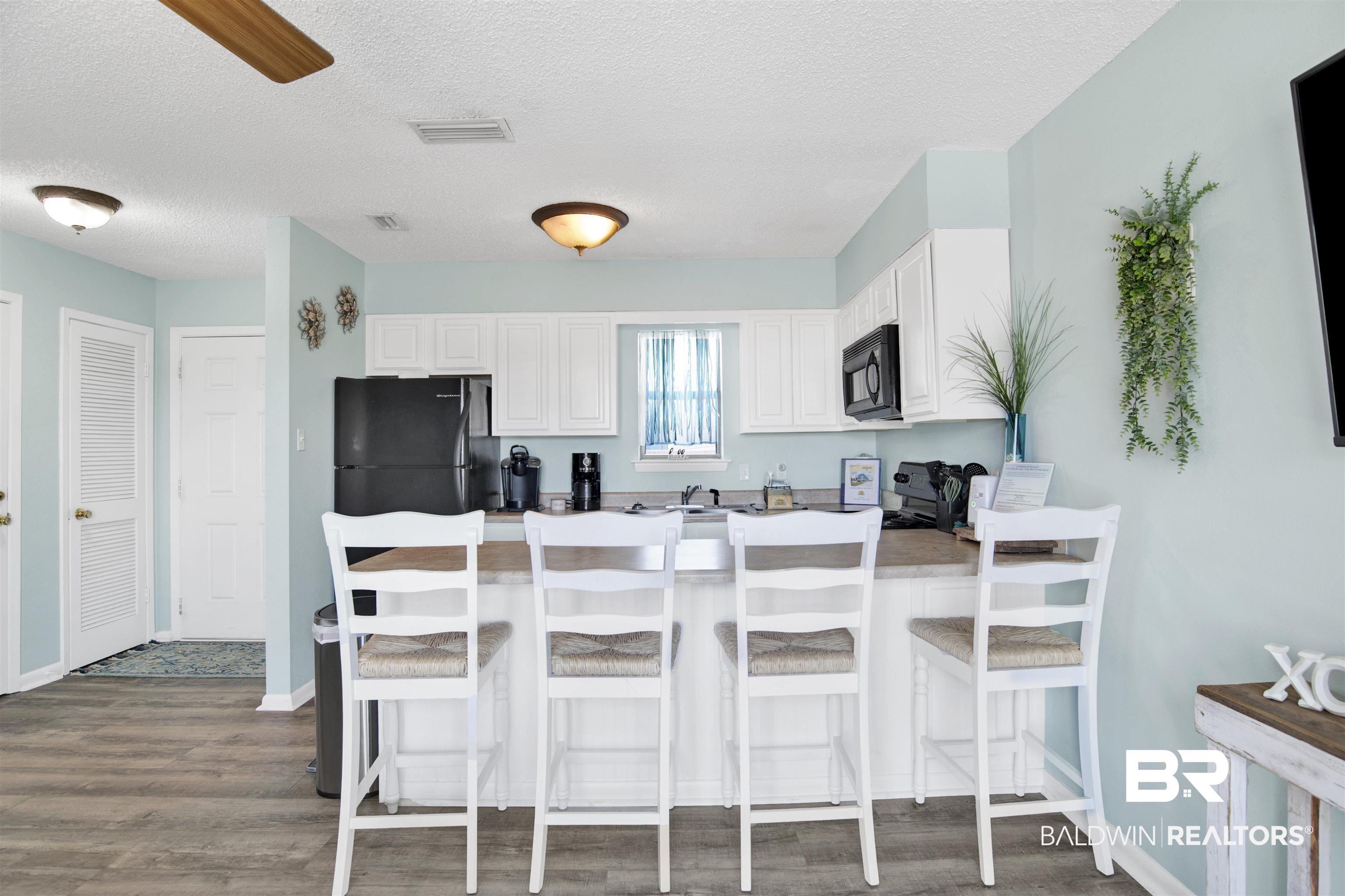 Image 3: Kitchen with a peninsula, a textured ceiling, wood finished floors, white cabinetry, and a kitchen breakfast bar