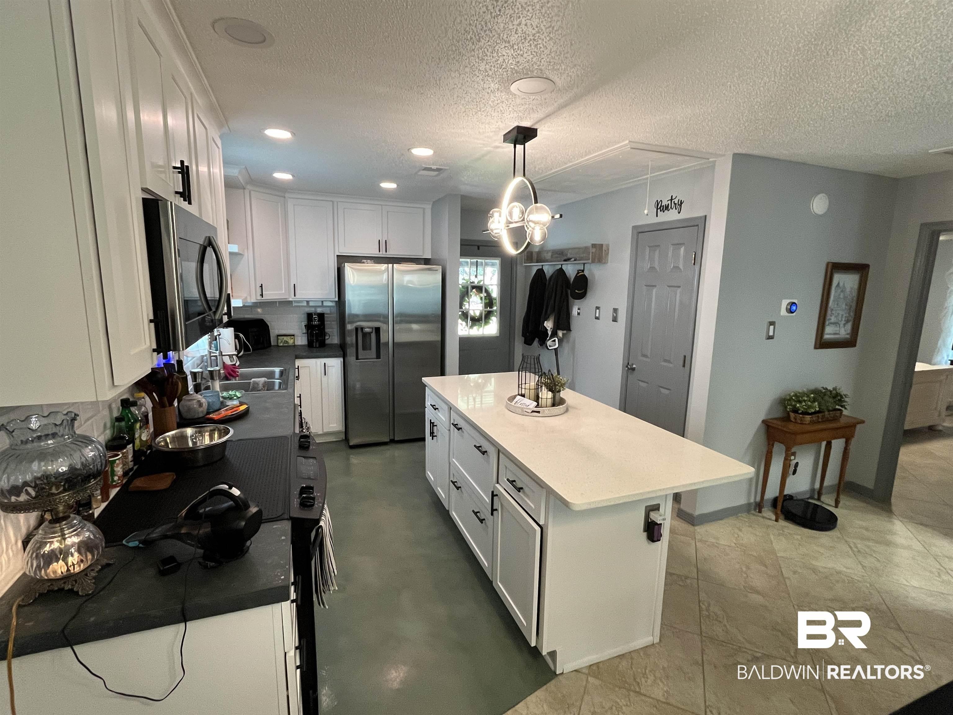 Image 3: Kitchen featuring white cabinetry, a central island with a light-colored countertop, and recessed lighting