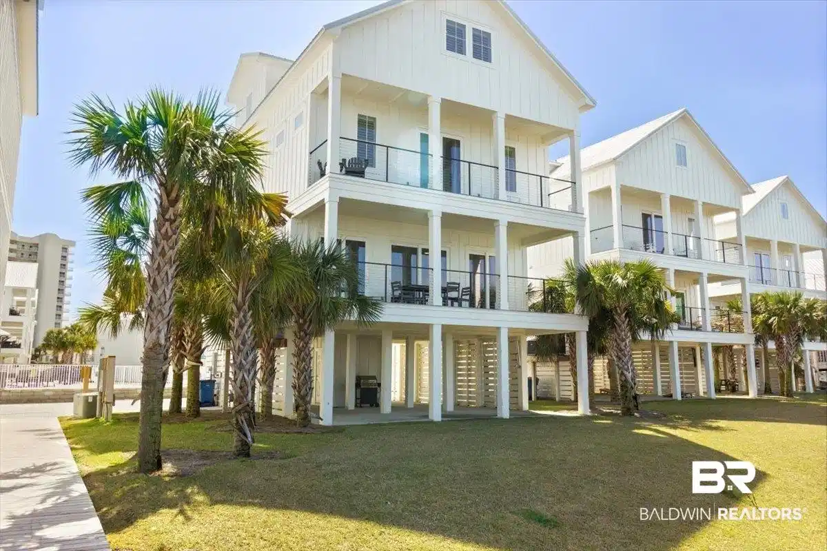Image 1: Coastal-style residence featuring white board and batten siding, multiple balconies with black railings, and a raised foundation