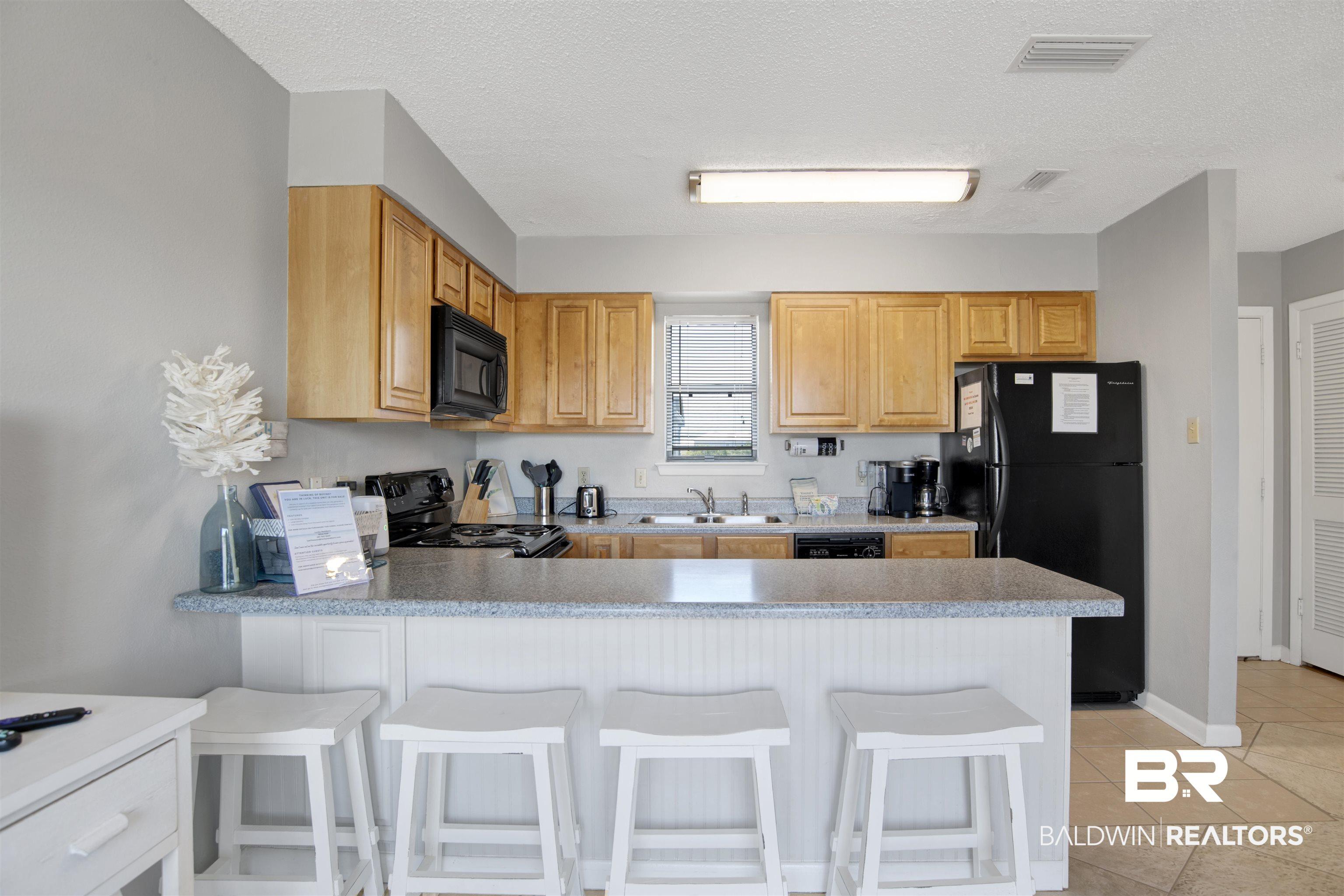 Image 3: Kitchen with black appliances, a peninsula, light tile patterned floors, a kitchen breakfast bar, and light countertops