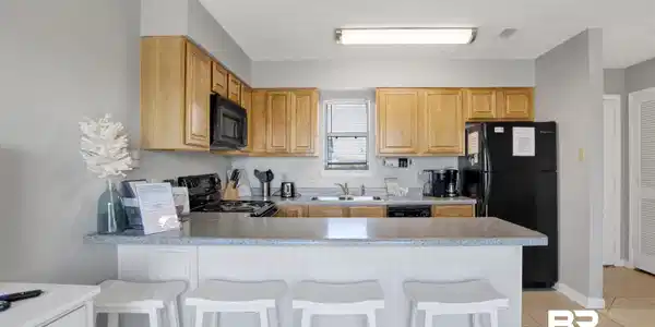 Image 3: Kitchen with black appliances, a peninsula, light tile patterned floors, a kitchen breakfast bar, and light countertops