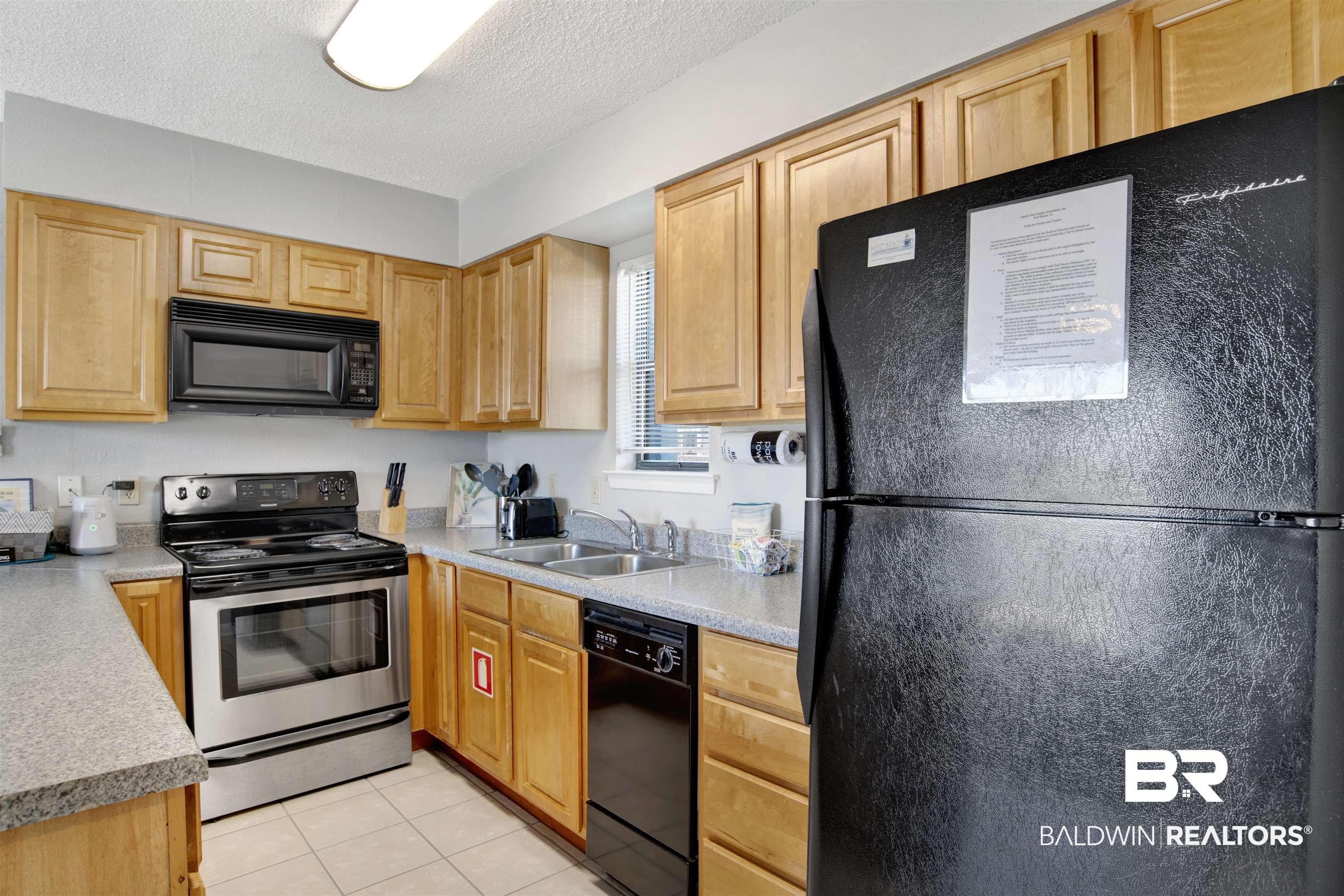 Image 4: Kitchen with black appliances, light countertops, a textured ceiling, light tile patterned floors, and light brown cabinetry