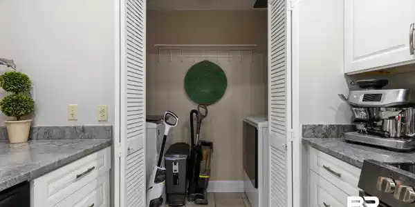 Image 4: Integrated laundry closet with louvered bi-fold doors, tiled flooring, and a wire shelf