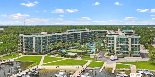 Image 2: Expansive waterfront condominium complex featuring multiple residential buildings, a marina with numerous boat slips, a central pool area with landscaping, a putting green, and direct water access