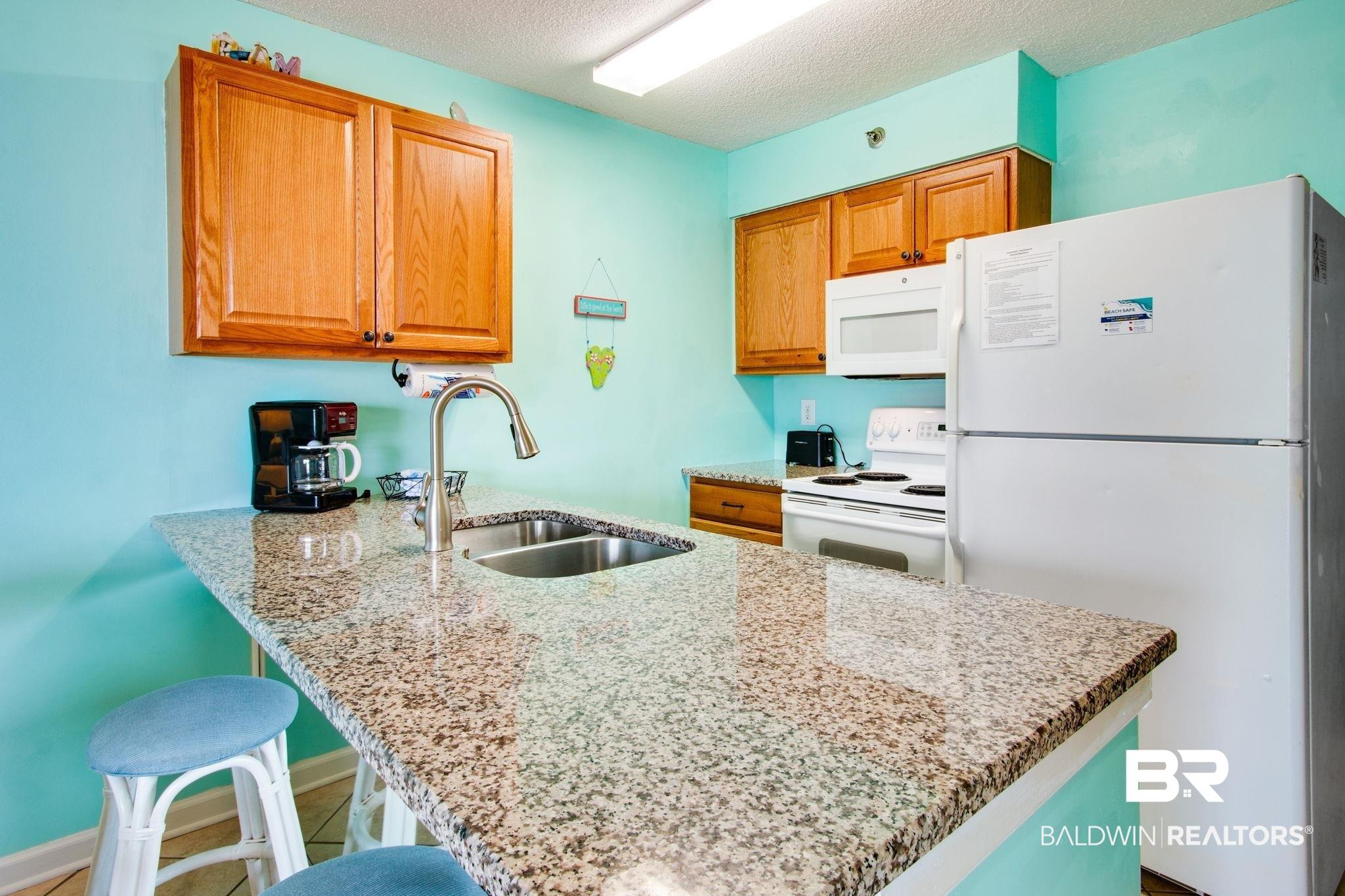 Image 2: Kitchen with a peninsula, white appliances, light stone countertops, a kitchen breakfast bar, and brown cabinetry