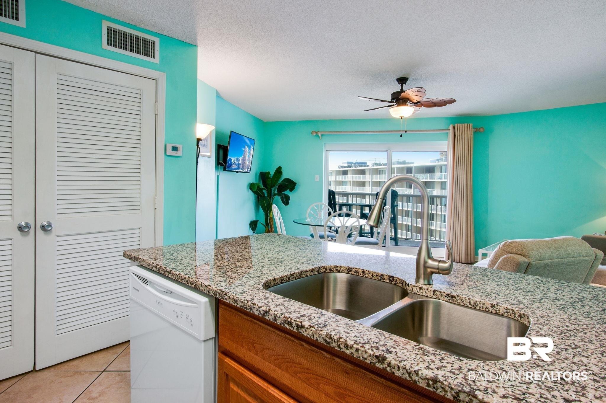 Image 3: Kitchen featuring brown cabinetry, white dishwasher, a textured ceiling, light stone countertops, and light tile patterned floors