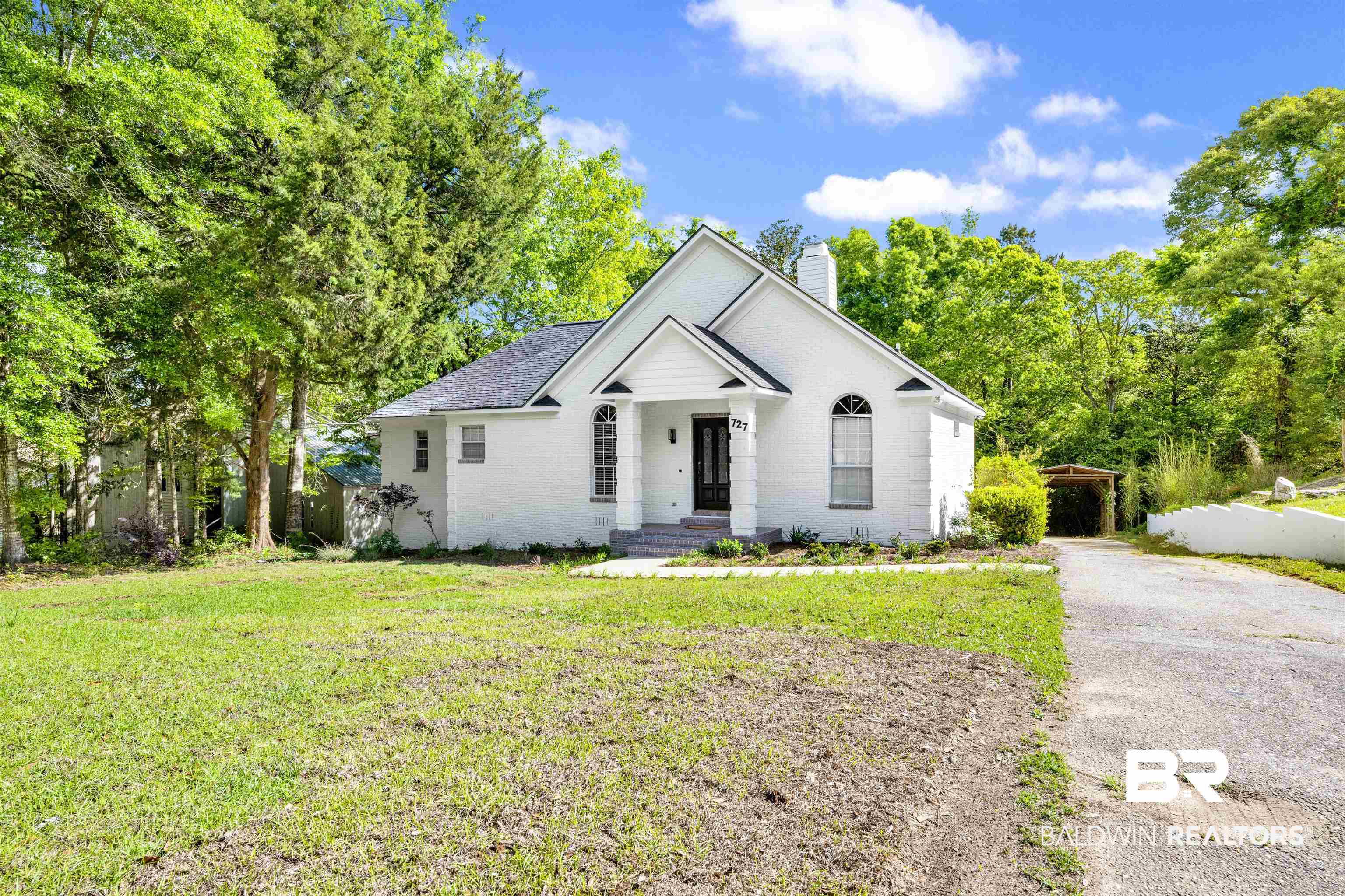 Image 3: View of front of property with a chimney, brick siding, covered porch, a front lawn, and view of scattered trees