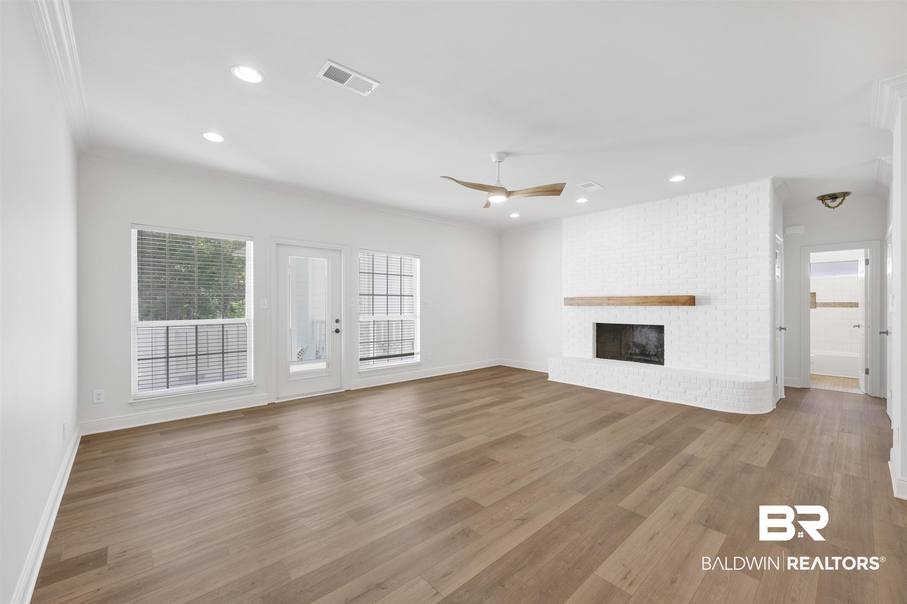 Image 4: Unfurnished living room featuring a ceiling fan, dark wood-type flooring, a brick fireplace, recessed lighting, and crown molding