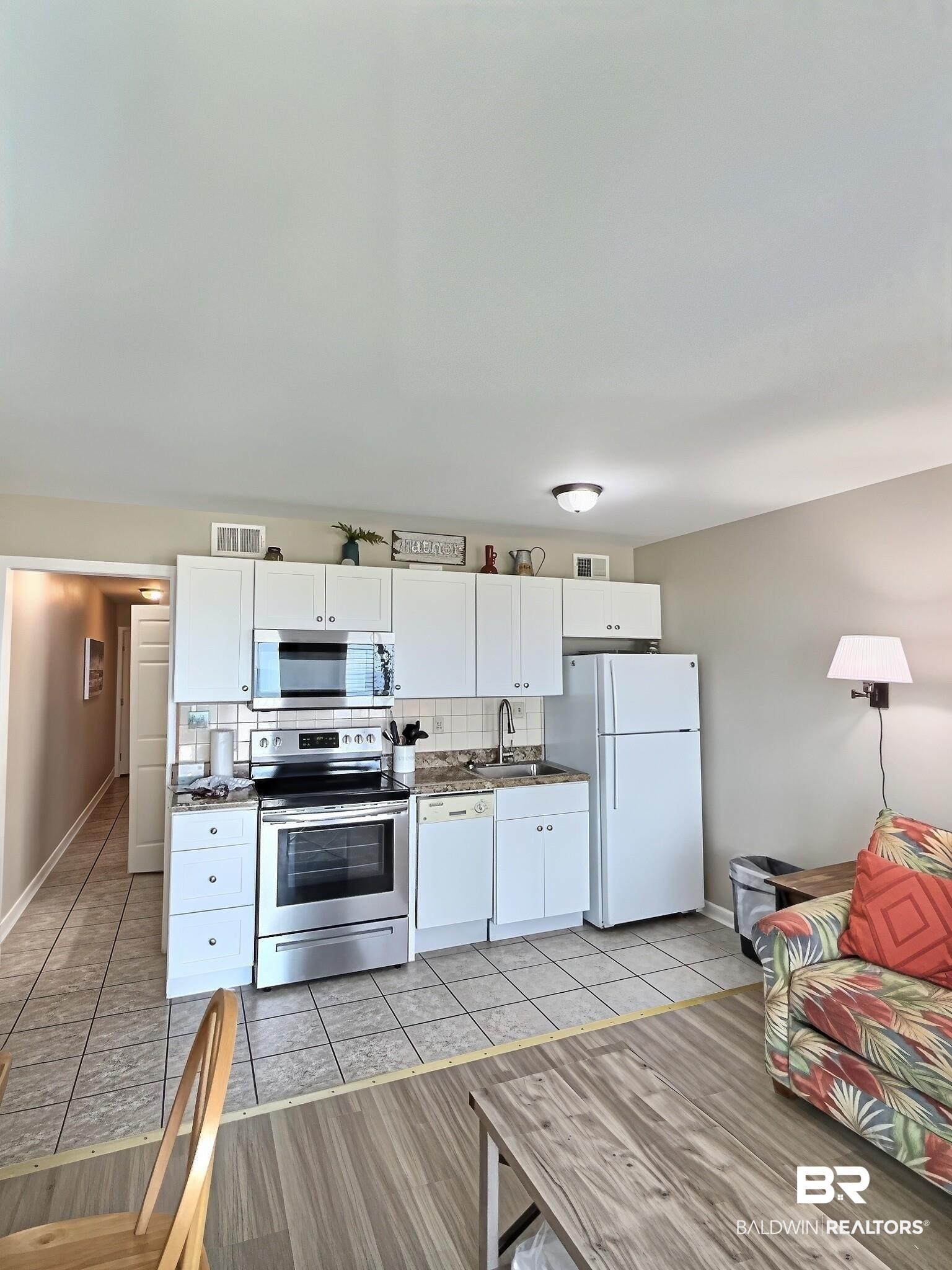Image 3: Compact kitchen featuring white cabinetry, stainless steel range and microwave, a white dishwasher, and a white refrigerator