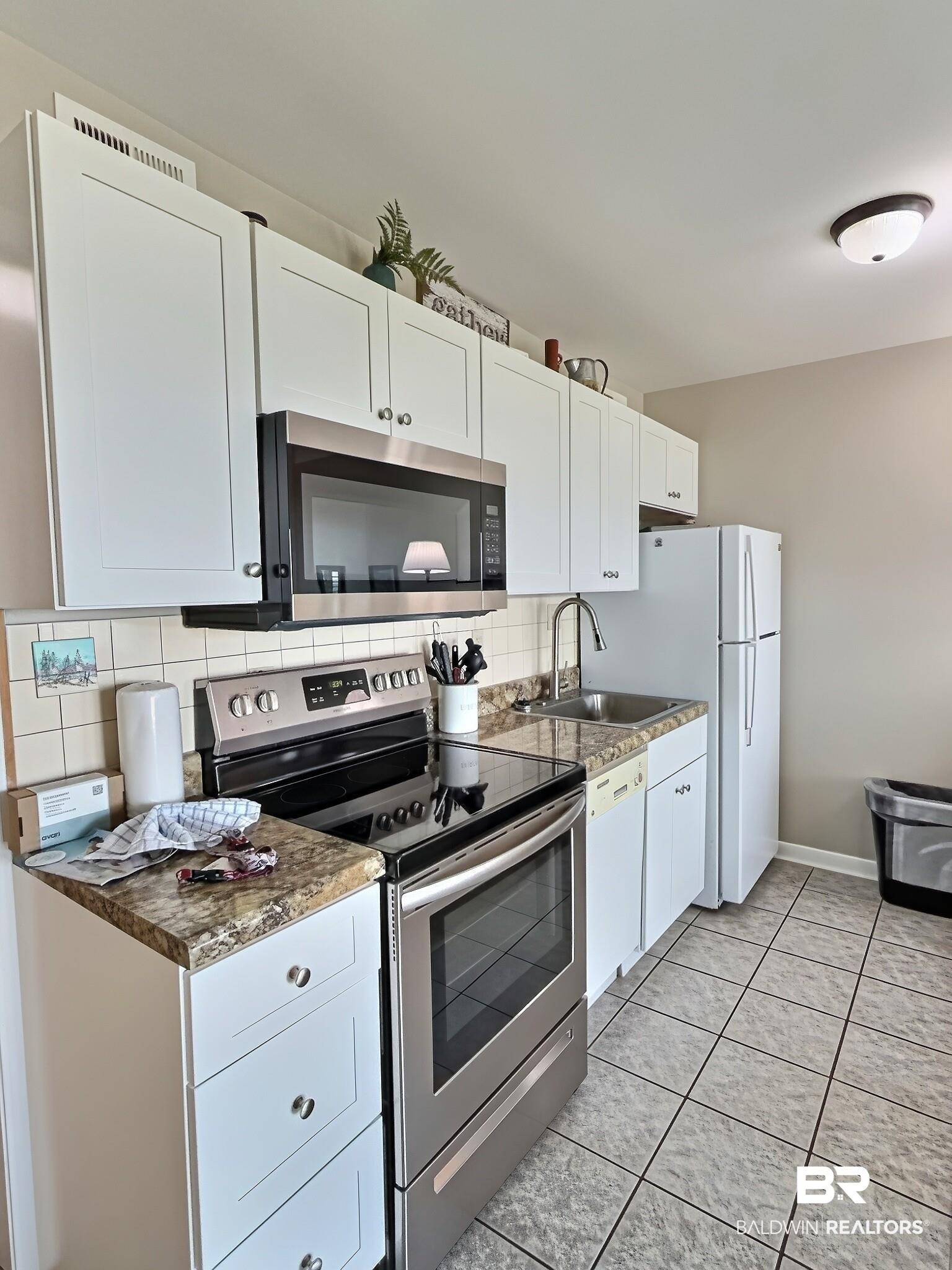 Image 4: Kitchen featuring white cabinetry, a stainless steel over-the-range microwave, a stainless steel electric range, a stainless steel sink, and light-toned square tile flooring