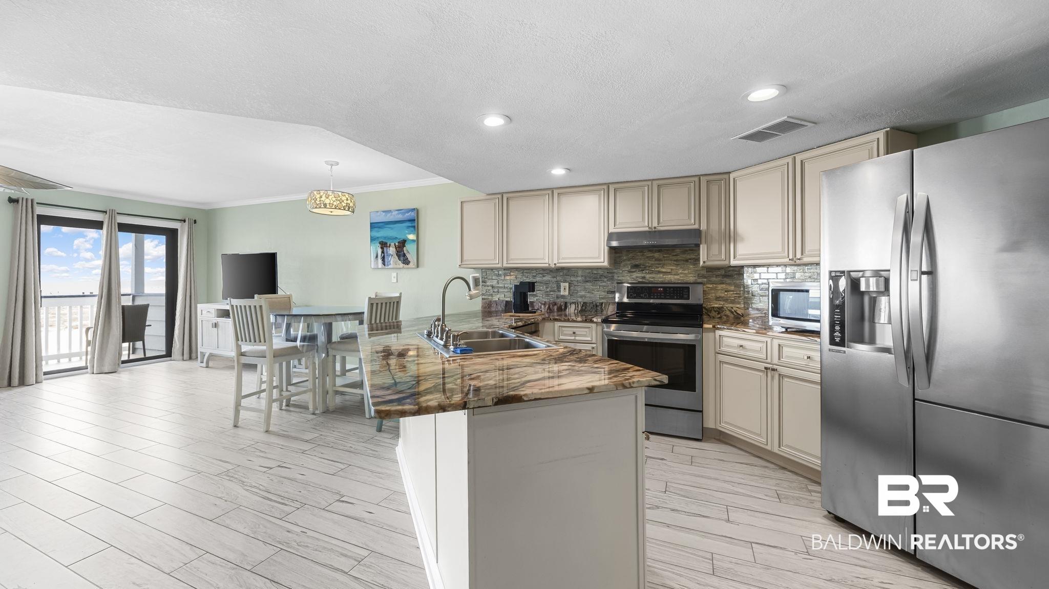 Image 4: Kitchen featuring stainless steel appliances, crown molding, dark stone counters, decorative backsplash, and a kitchen breakfast bar