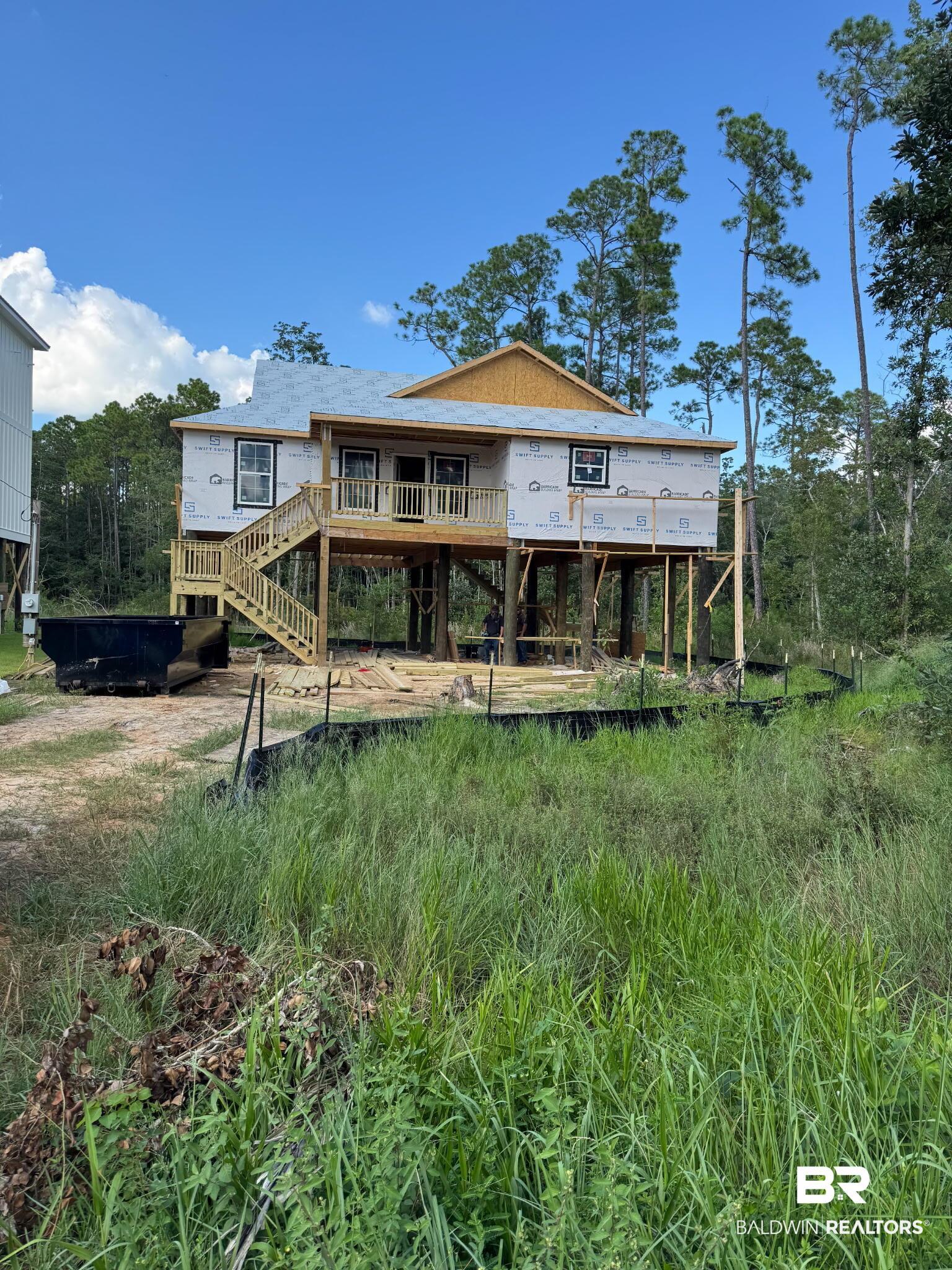 Image 2: New construction elevated home featuring a second-story balcony with wood railings, exterior wood stairs, and multiple windows