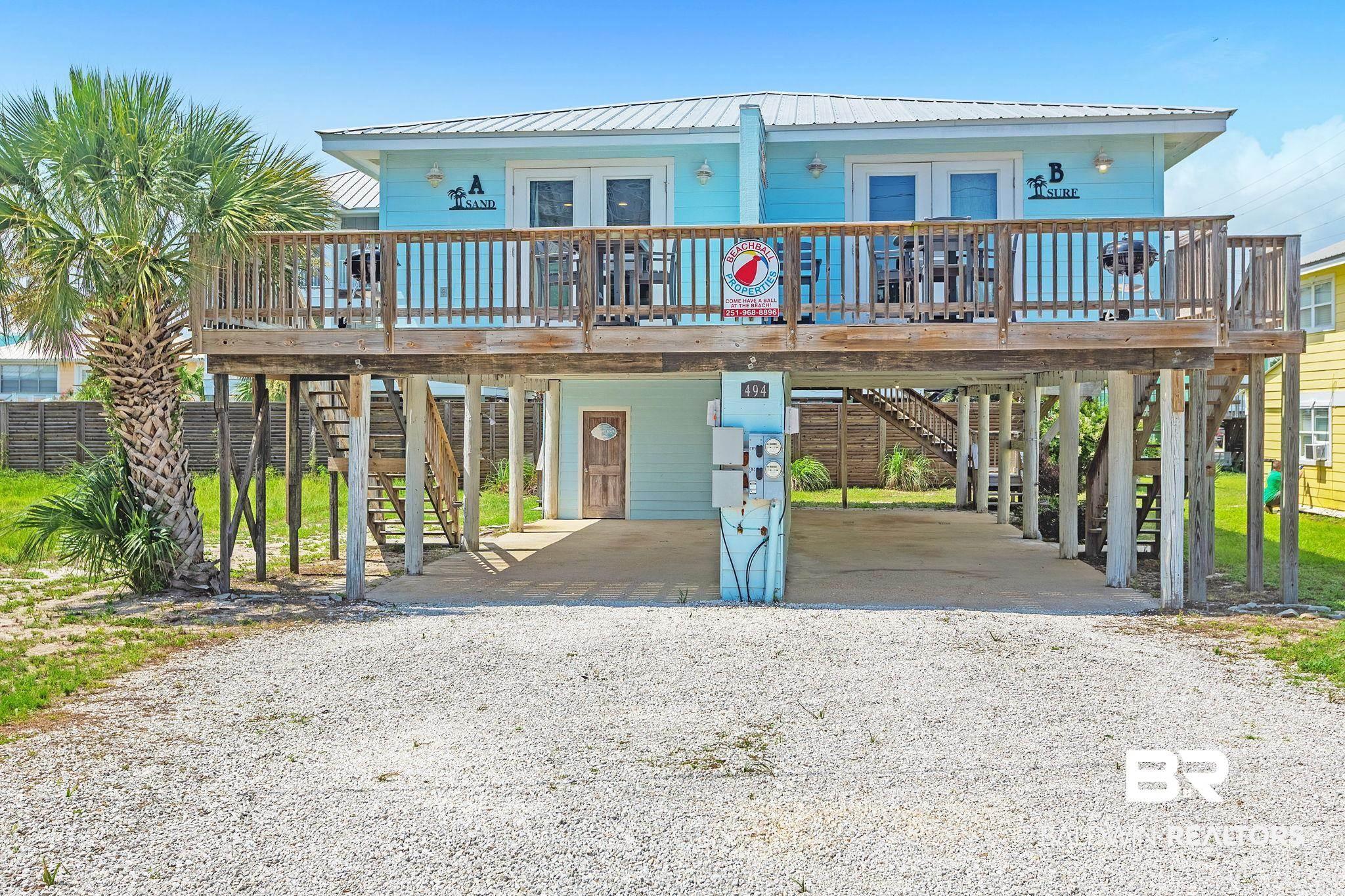 Image 1: Elevated coastal-style duplex featuring a light blue exterior, white trim, and a metal roof