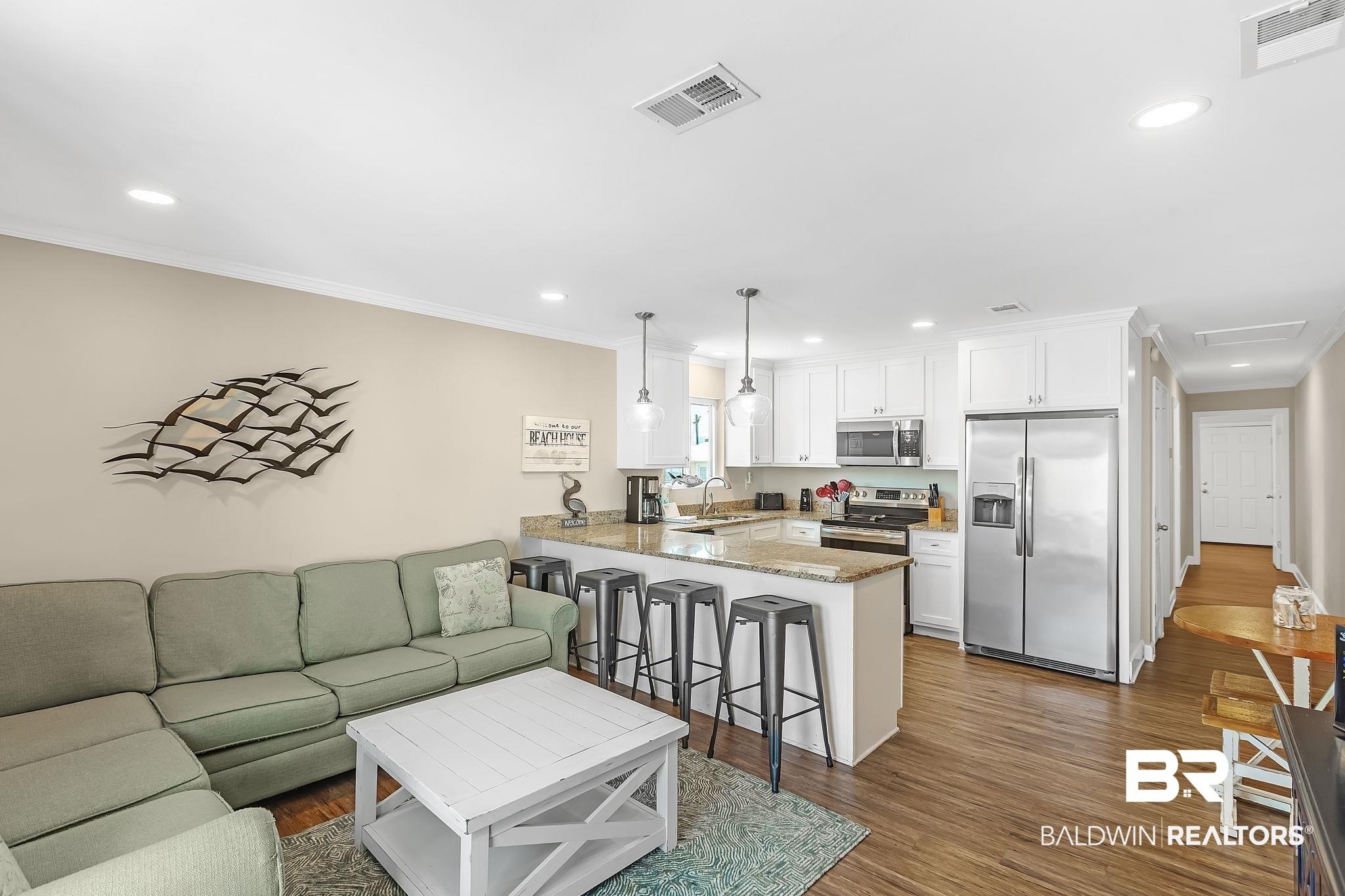 Image 3: Open-concept living area featuring wood-finish flooring, white crown molding, and recessed lighting