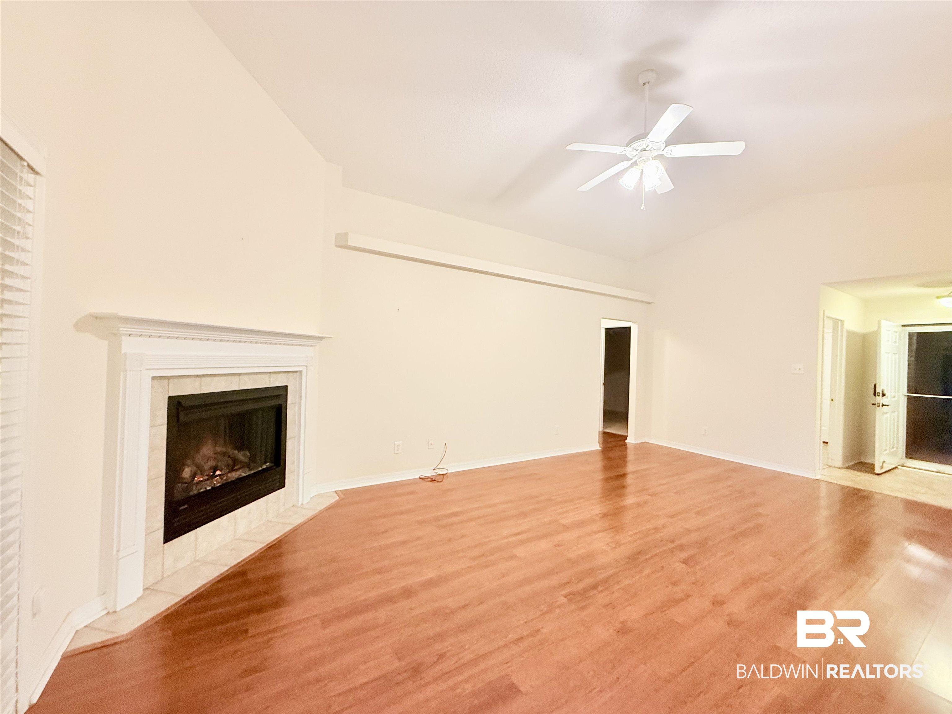 Image 3: Spacious interior featuring wood-finish flooring, a vaulted ceiling, and a ceiling fan with light fixture