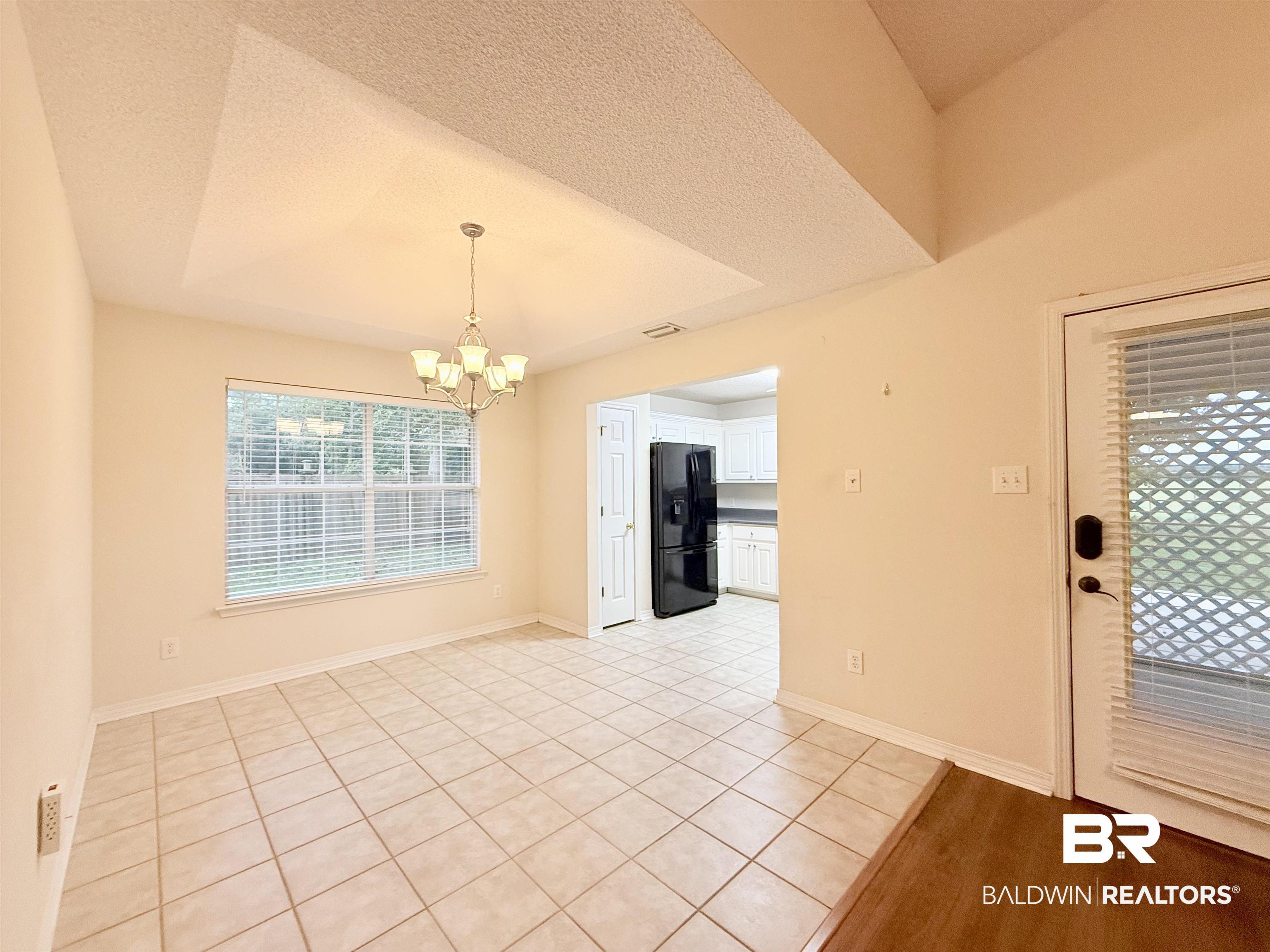 Image 4: Dining area featuring a vaulted ceiling with a central chandelier, a large window with blinds, and neutral-toned tile flooring