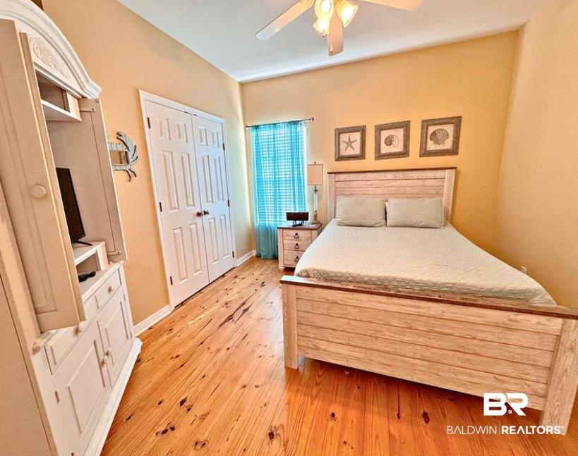 Image 3: Bedroom featuring natural wood-finish flooring, a ceiling fan, and a double-door closet