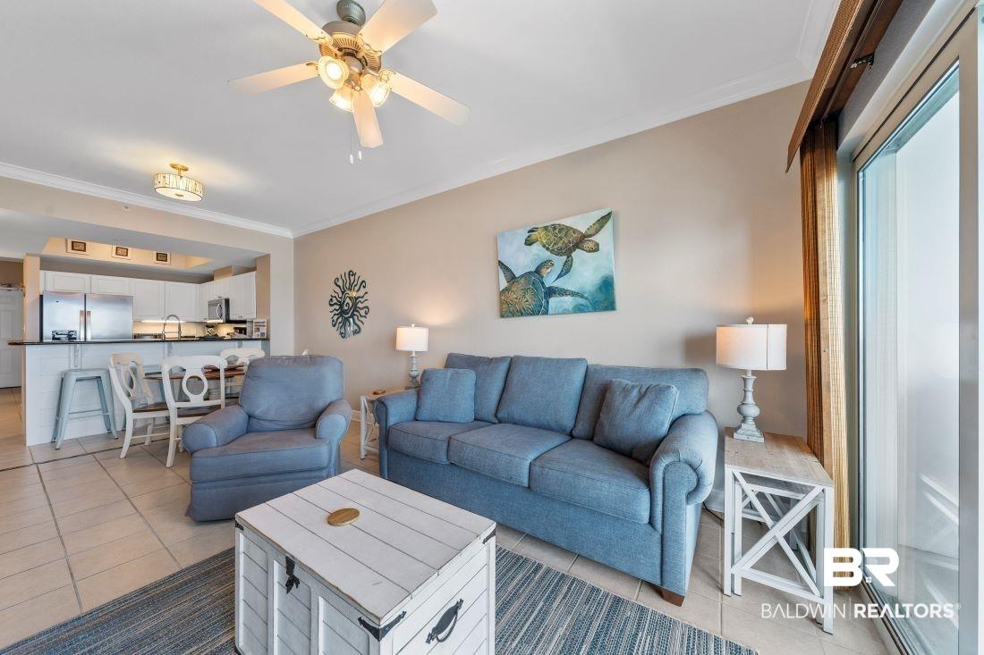 Image 4: Living room with crown molding, light tile patterned floors, and ceiling fan
