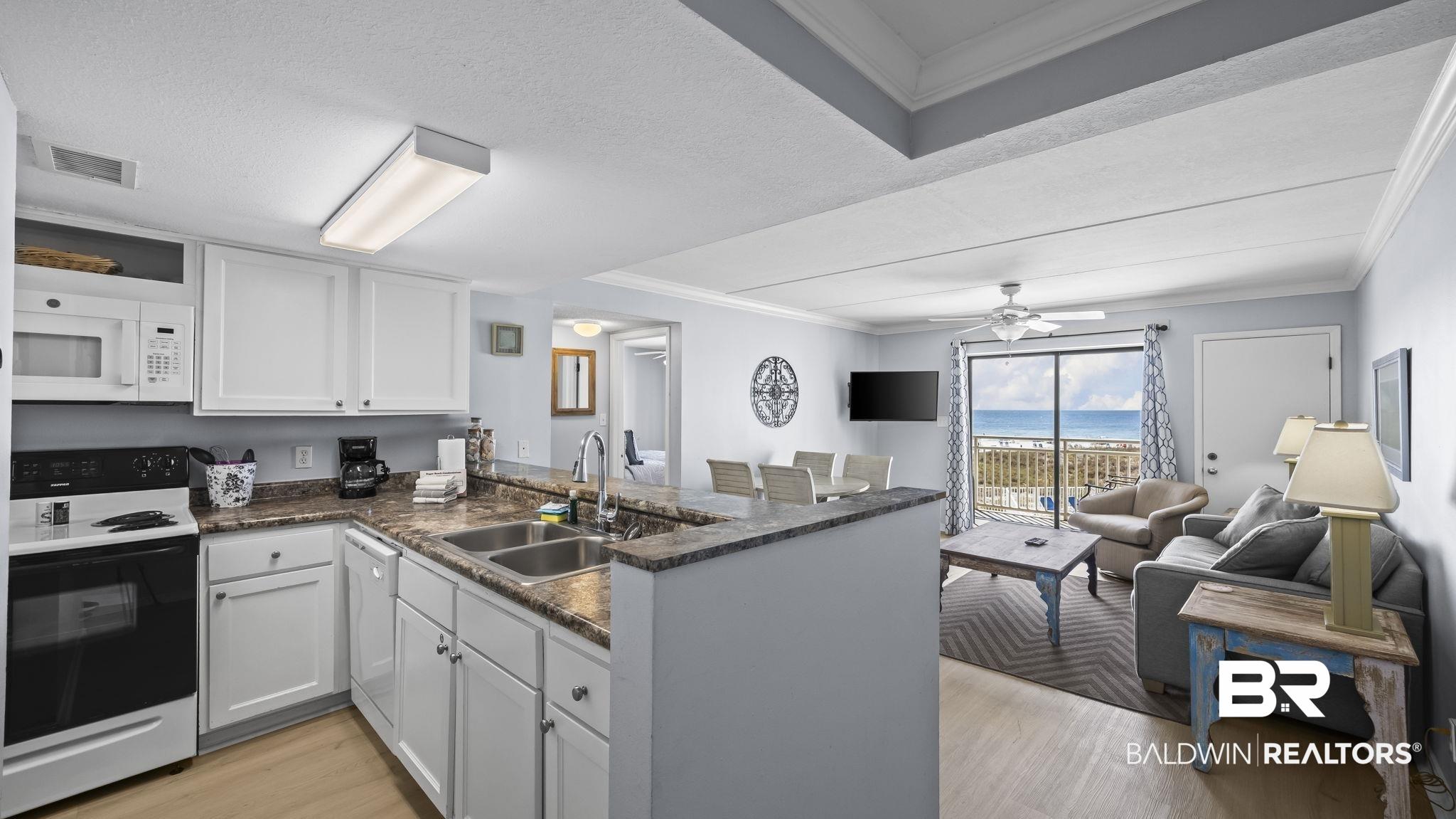 Image 2: Kitchen featuring white appliances, crown molding, light wood-type flooring, a peninsula, and white cabinetry
