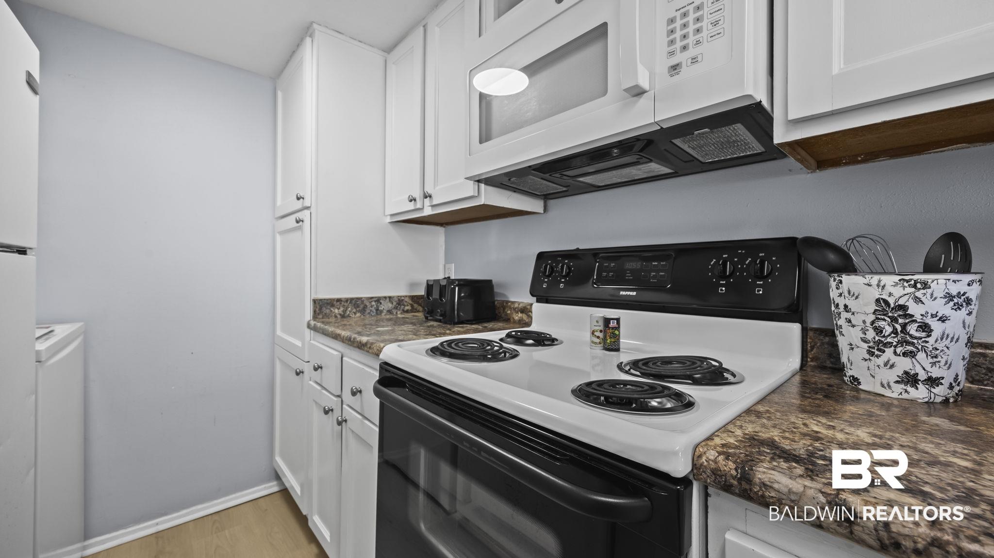 Image 3: Kitchen with white appliances, dark countertops, white cabinetry, light wood-style flooring, and washer / clothes dryer