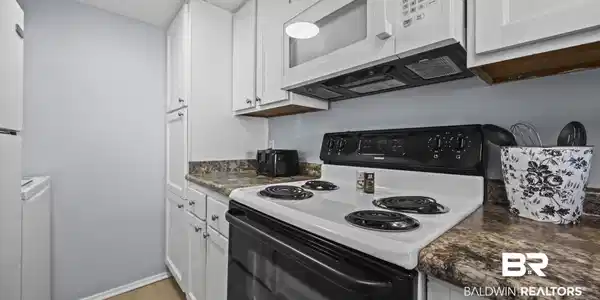 Image 3: Kitchen with white appliances, dark countertops, white cabinetry, light wood-style flooring, and washer / clothes dryer