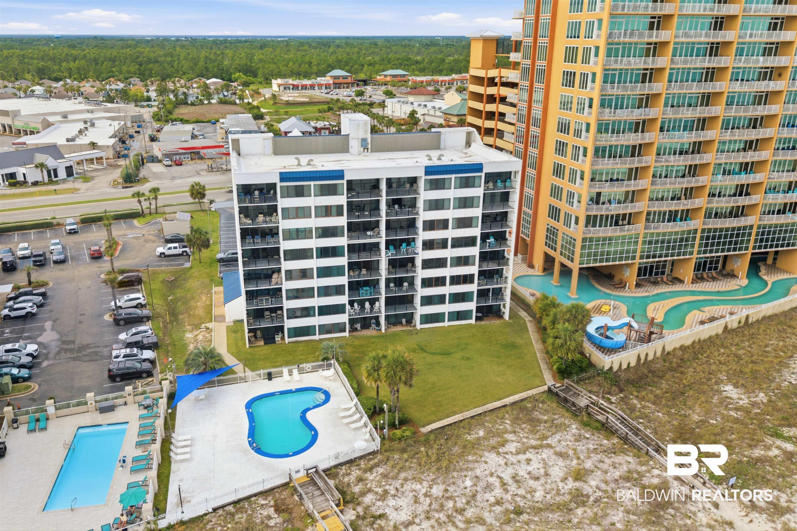 Image 1: Coastal high-rise property featuring multiple swimming pools, a wooden boardwalk, and surrounding green spaces