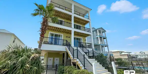 Image 2: Multi-story residence featuring a pale yellow exterior, multiple balconies with black railings, and a prominent palm tree
