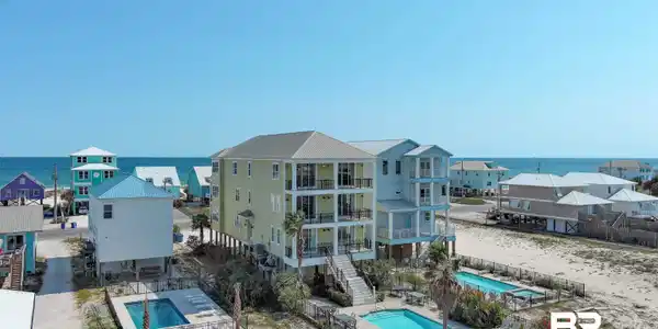 Image 4: Coastal-style architecture featuring multiple balconies, a metal roof, two outdoor swimming pools, and a separate single-story pool with a surrounding fence
