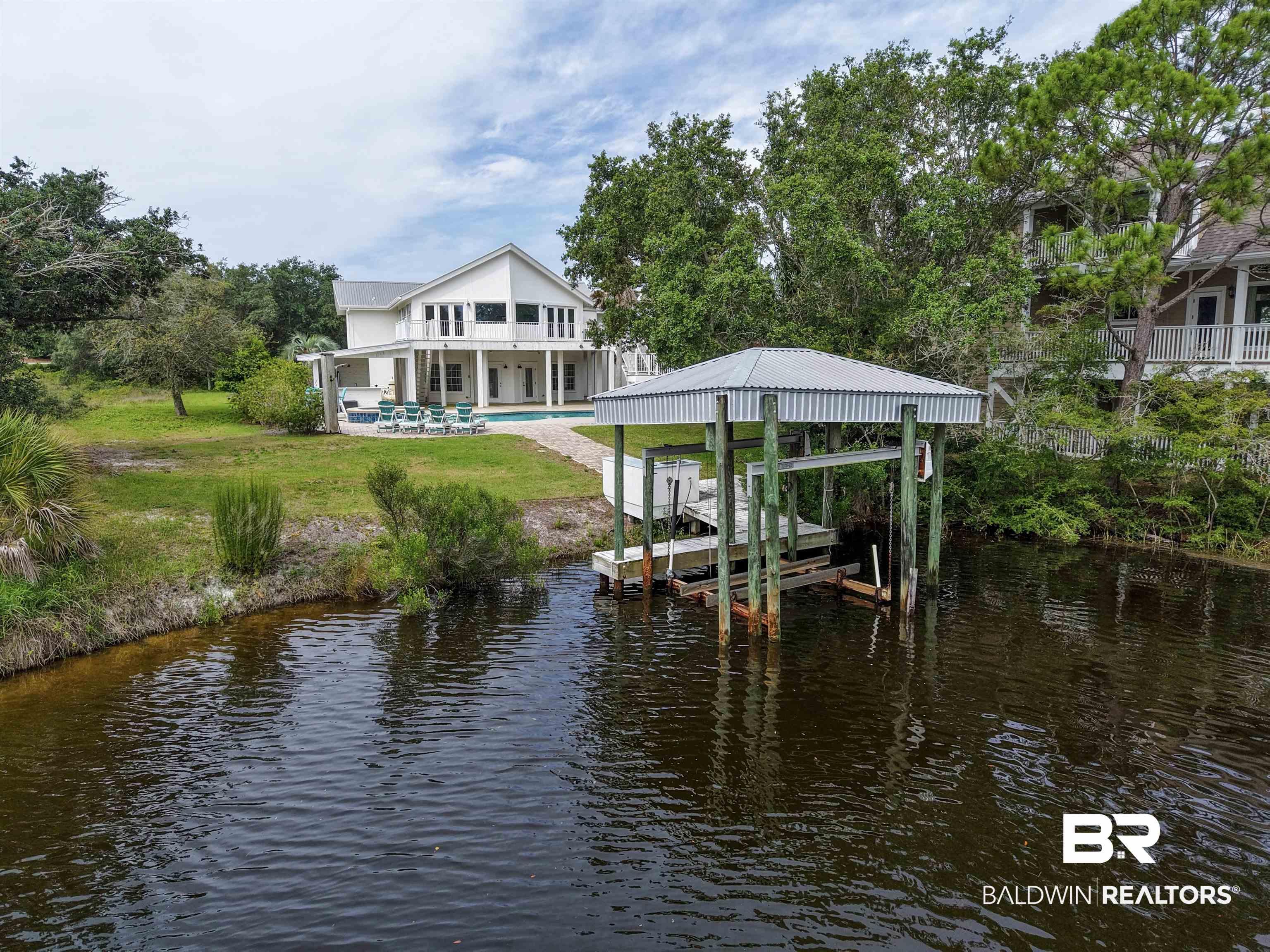 Image 3: Waterfront property featuring a private boat dock with covered lift, a white exterior residence with multiple balconies, a ground-level covered patio, and an in-ground swimming pool