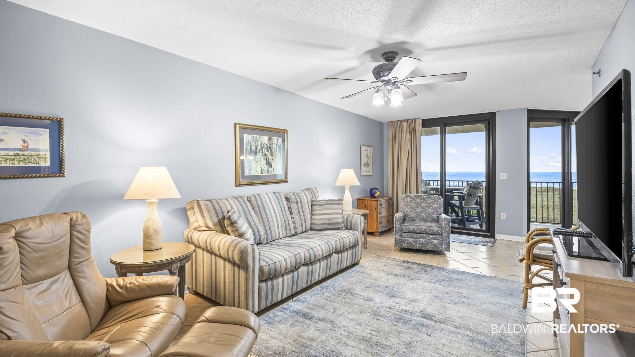 Image 3: Spacious living area featuring light blue walls, ceramic tile flooring, a ceiling fan with integrated lighting, and direct access to an outdoor balcony