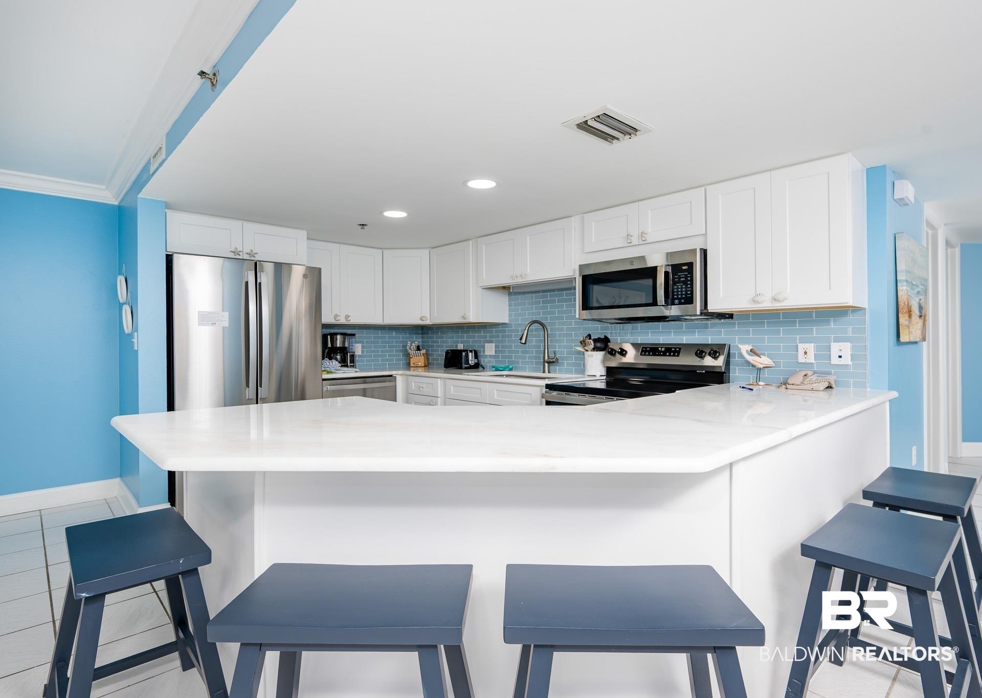 Image 2: Kitchen featuring white cabinets, stainless steel appliances, a kitchen breakfast bar, light tile patterned floors, and recessed lighting