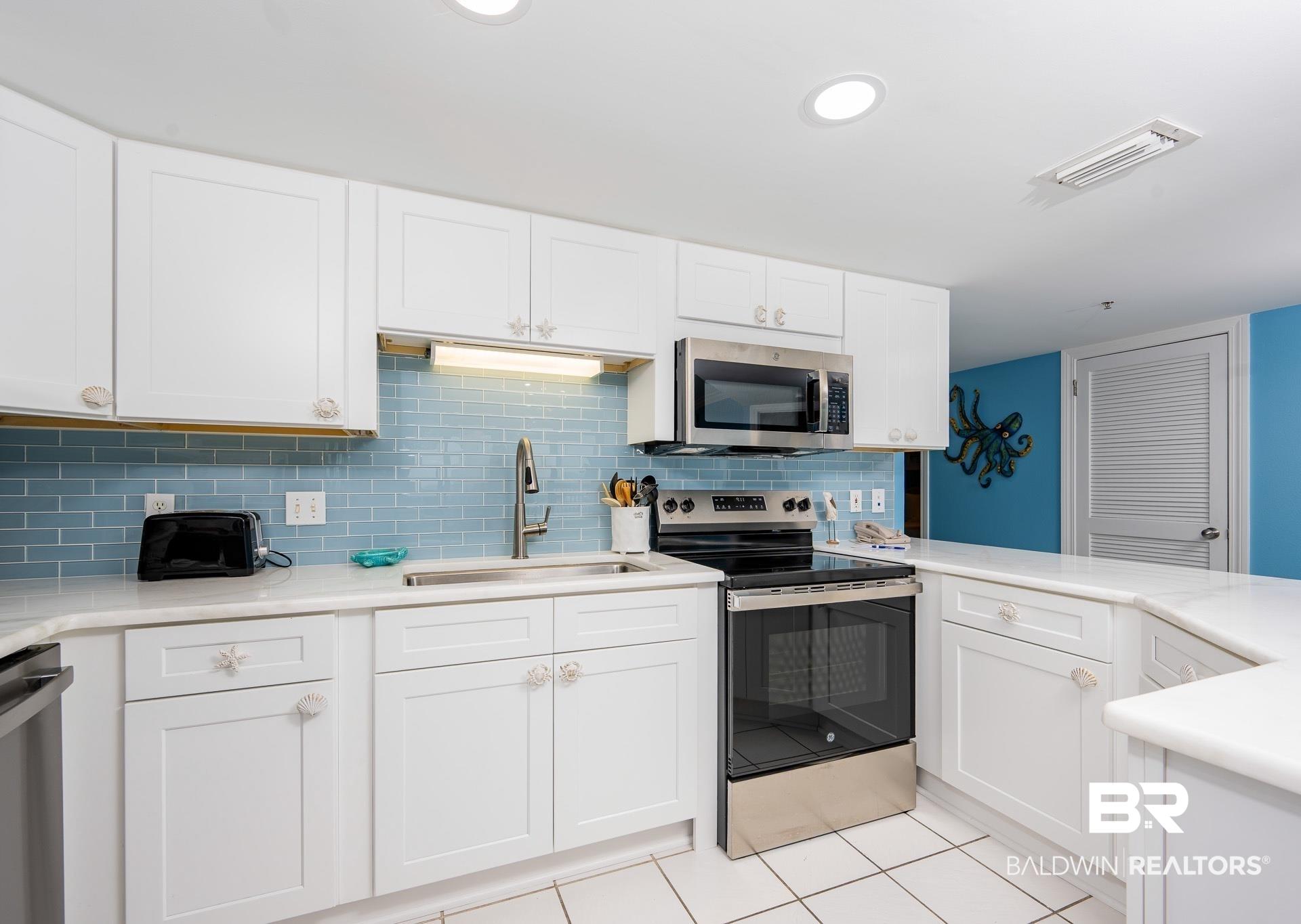 Image 3: Kitchen featuring appliances with stainless steel finishes, white cabinets, light tile patterned floors, light stone counters, and tasteful backsplash