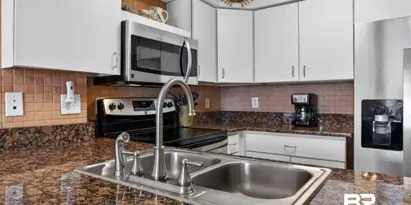 Image 4: Kitchen featuring a double-basin stainless steel sink with a high-arc faucet, granite countertops, tile backsplash, white cabinetry, and stainless steel appliances including a microwave, range, and refrigerator