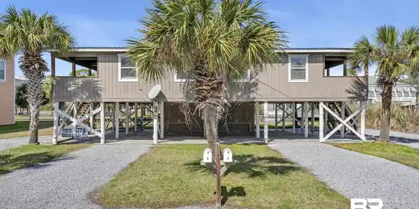 Image 4: Stilt-raised duplex featuring two separate gravel driveways, multiple mature palm trees, and a covered upper-level porch