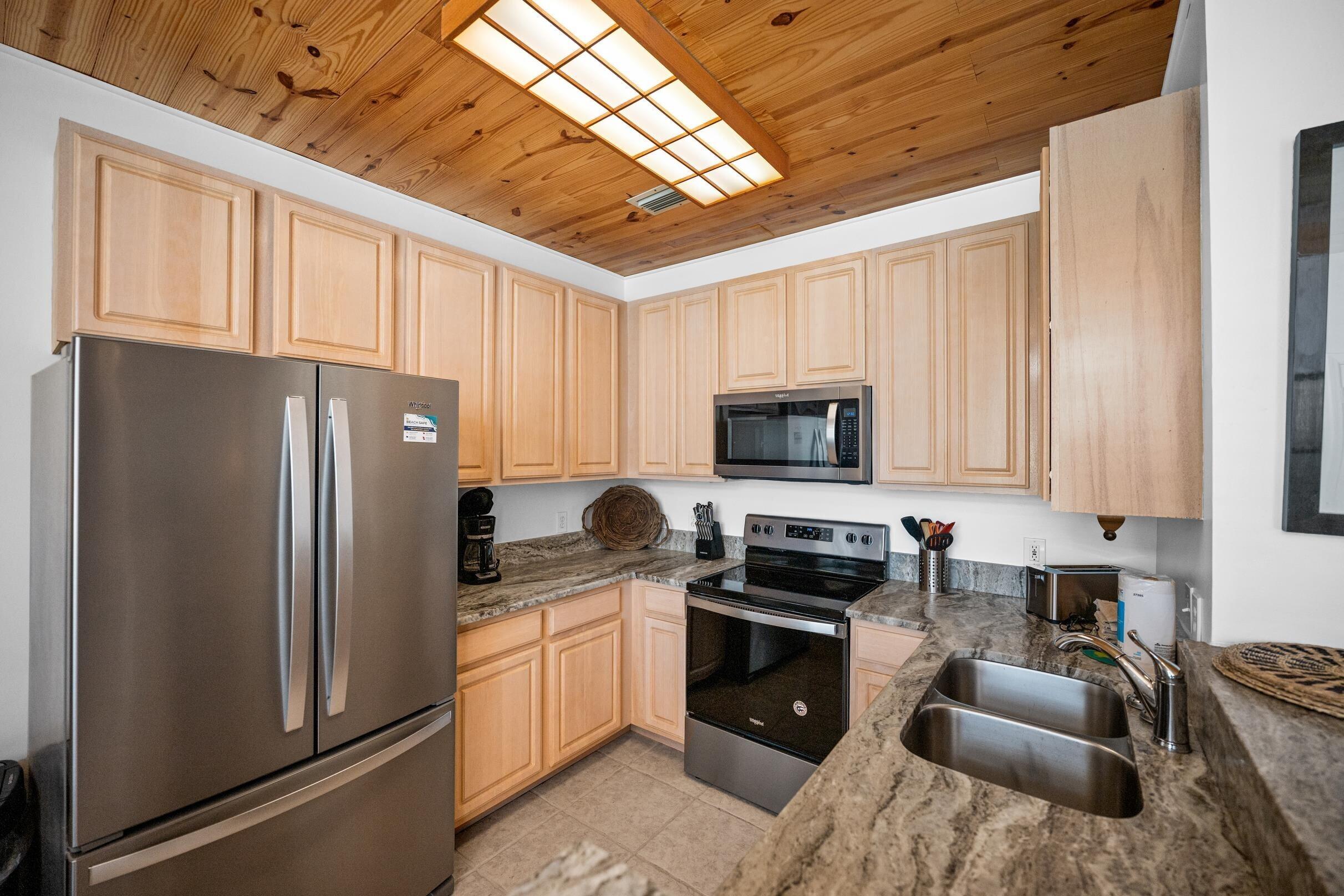 Image 4: Kitchen featuring appliances with stainless steel finishes, wooden ceiling, dark stone countertops, light brown cabinetry, and light tile patterned floors