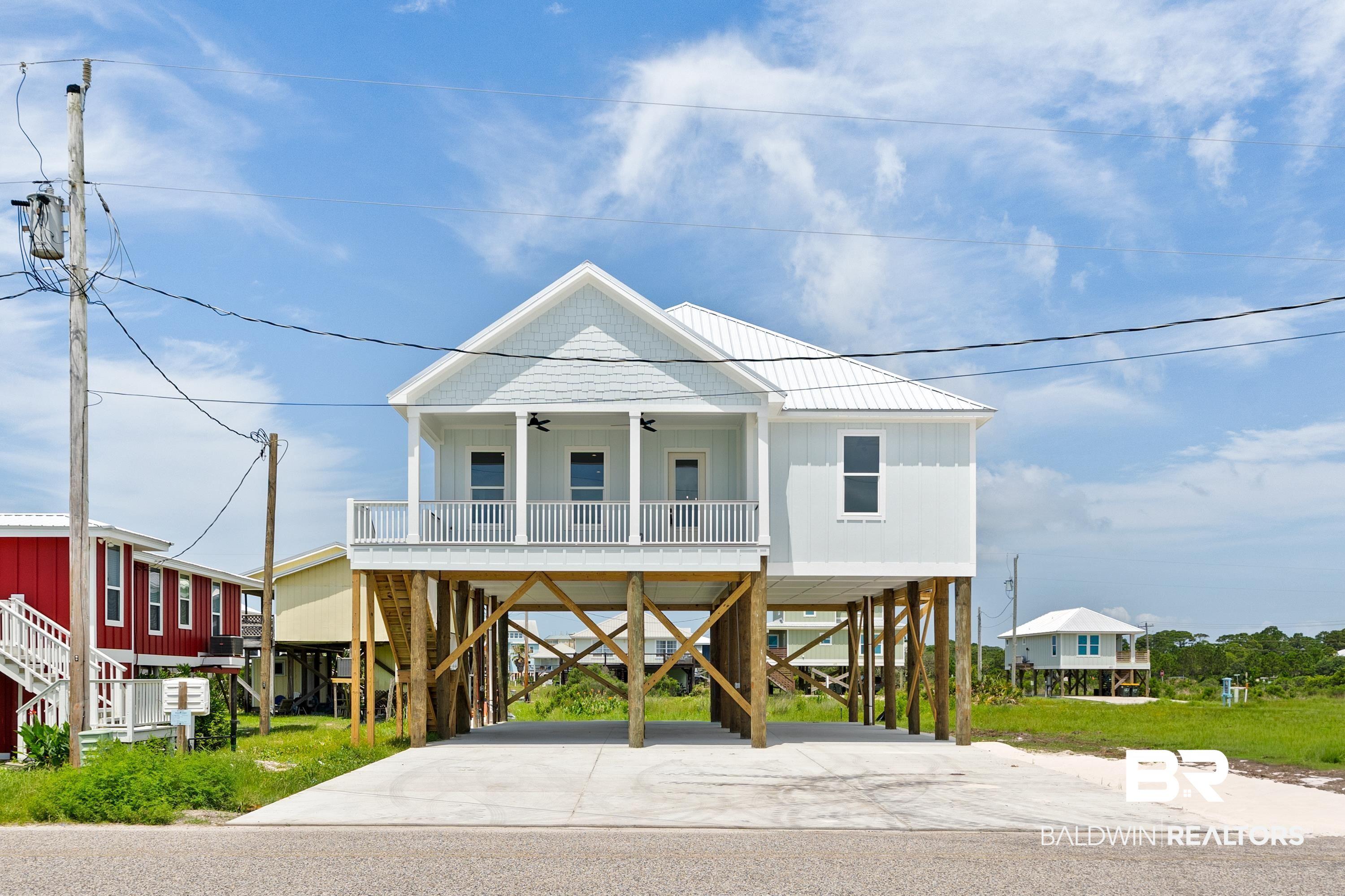 Image 1: Elevated coastal architecture featuring a white metal roof, light blue siding, and a covered porch with white railings