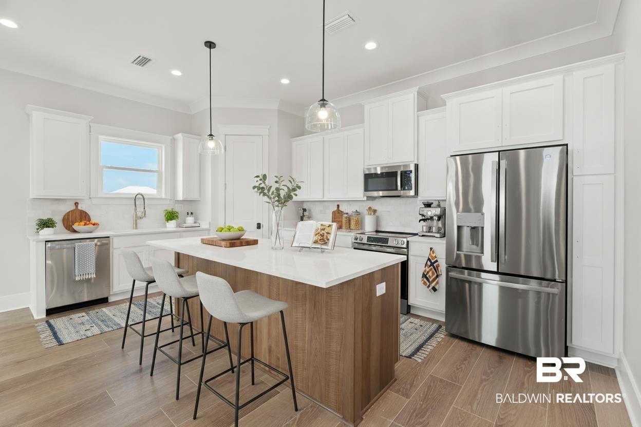 Image 4: Kitchen featuring a central island with countertop seating, white shaker cabinetry, stainless steel appliances, and wood-finish flooring