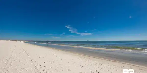 Image 4: Expansive sandy beach with clear blue water and bright blue skies