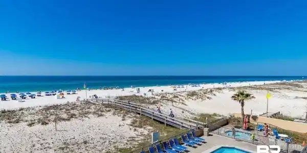 Image 2: Outdoor pool area with a hot tub, surrounded by lounge chairs, featuring a boardwalk pathway to the expansive white sand beach and ocean
