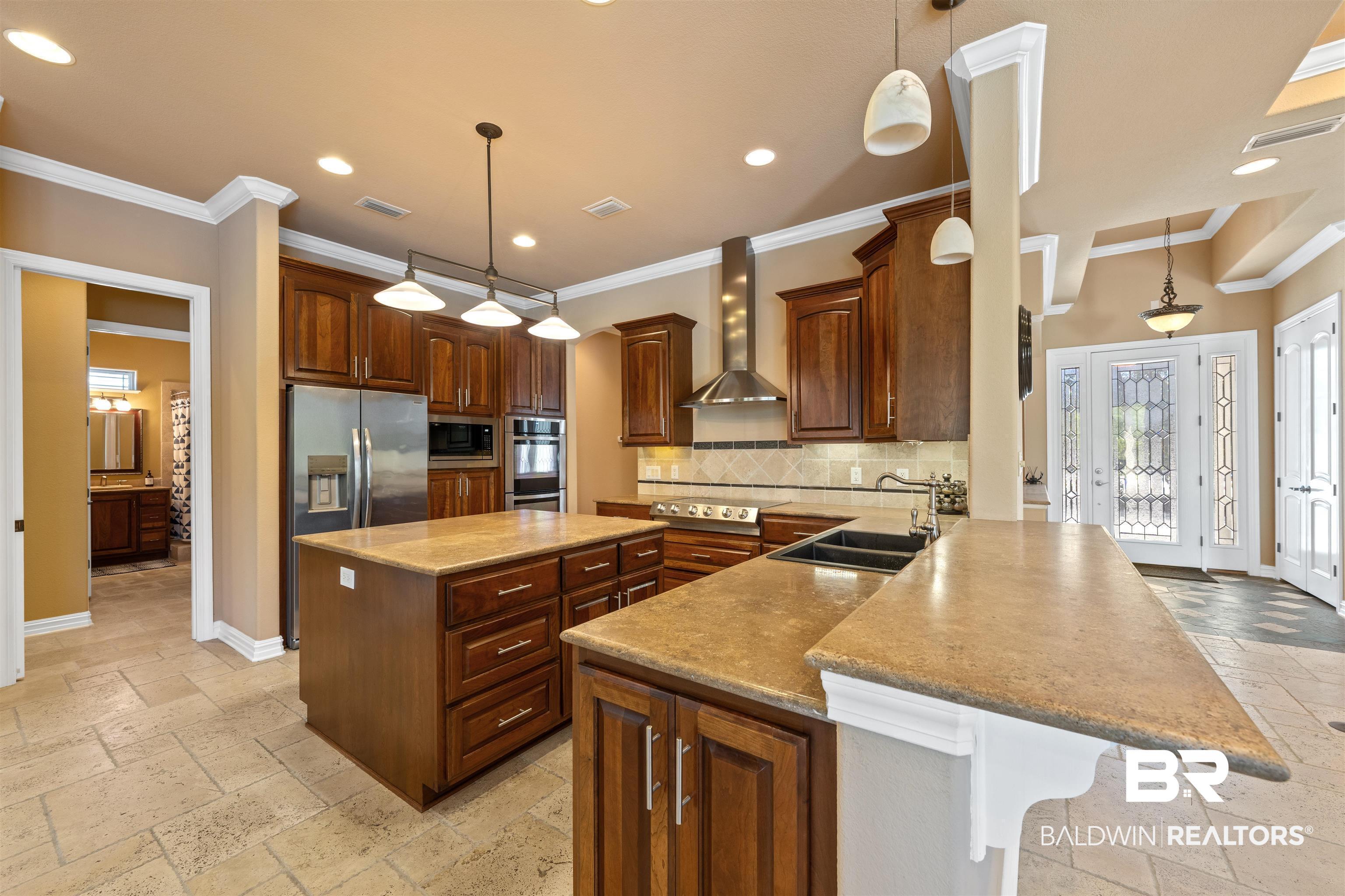 Image 3: Kitchen with stone tile floors, a kitchen island, a peninsula, decorative light fixtures, and crown molding