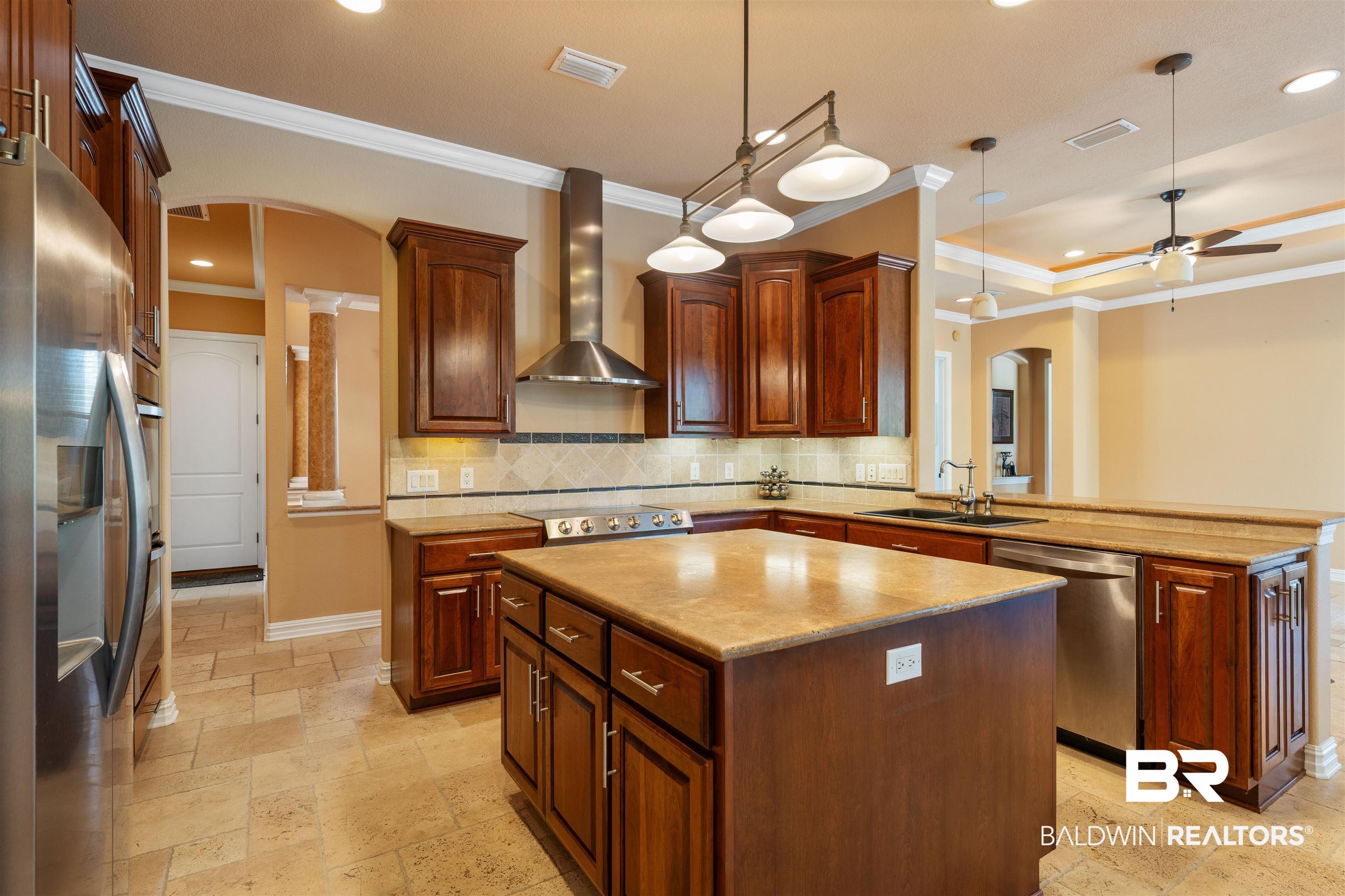 Image 4: Kitchen featuring arched walkways, a peninsula, a kitchen island, stone tile flooring, and crown molding