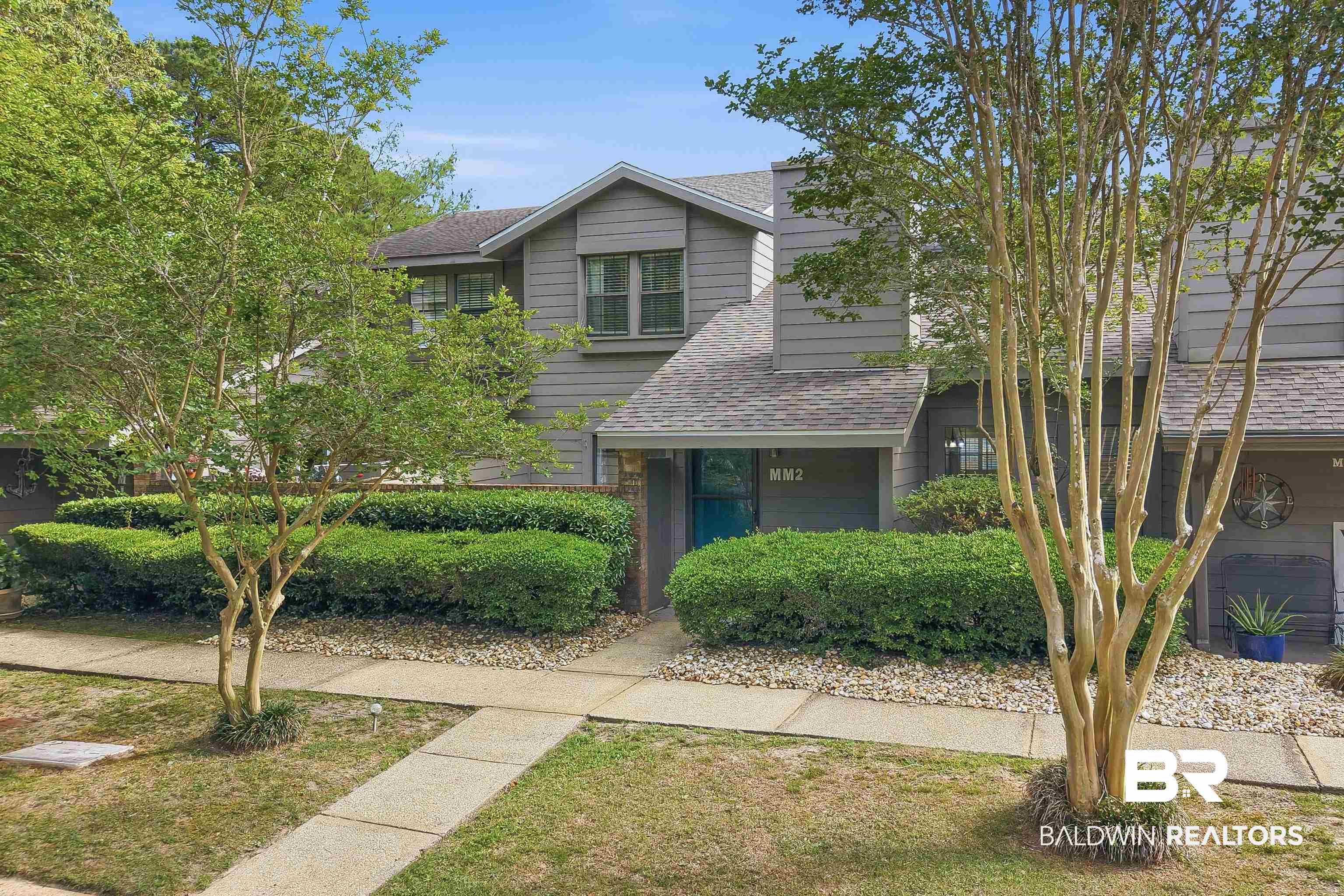 Image 2: Gray exterior with a blue entry door, accented by mature trees and manicured shrubbery
