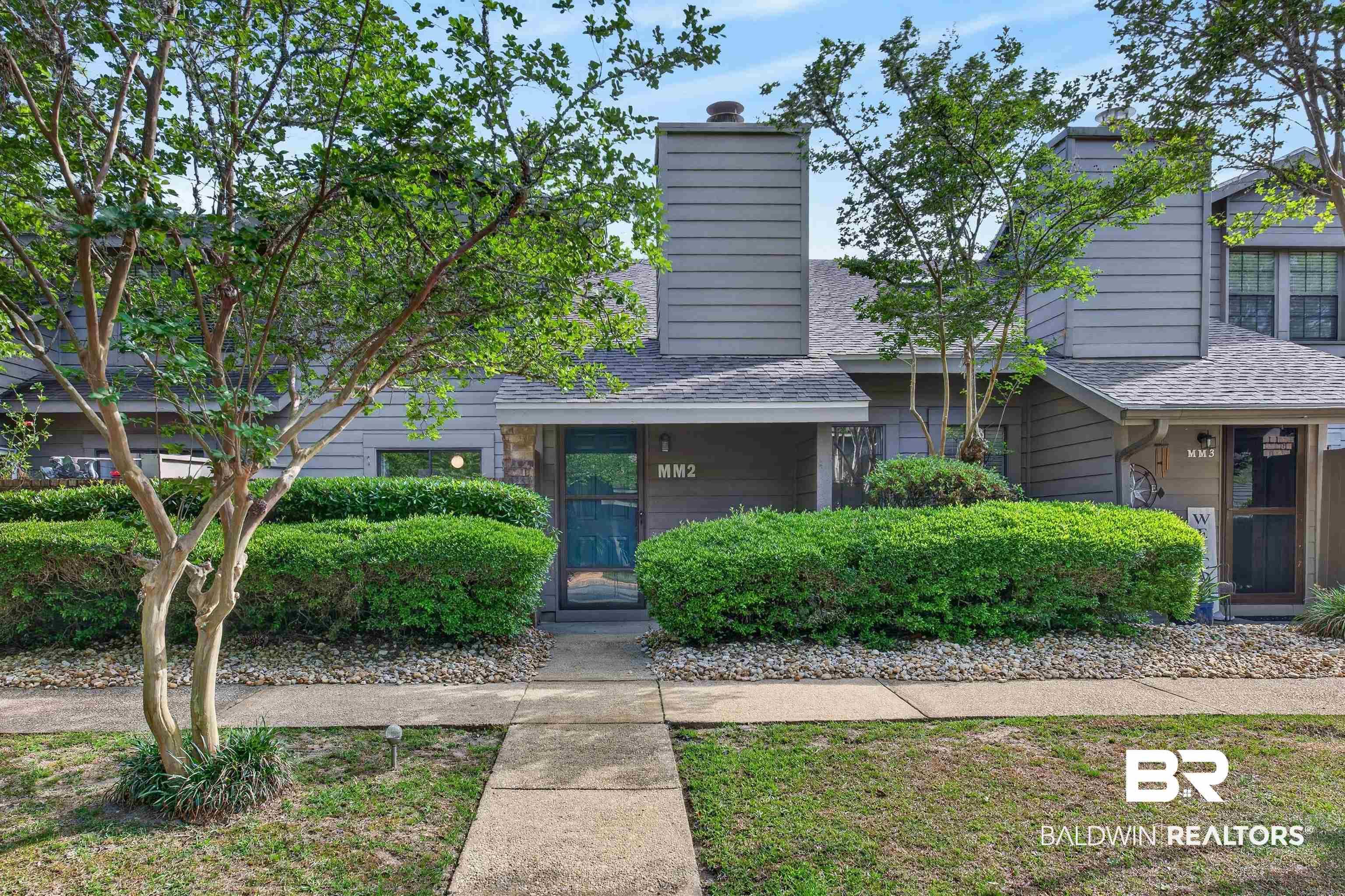 Image 4: Exterior featuring gray siding, a prominent chimney, mature trees, manicured hedges, and a concrete pathway