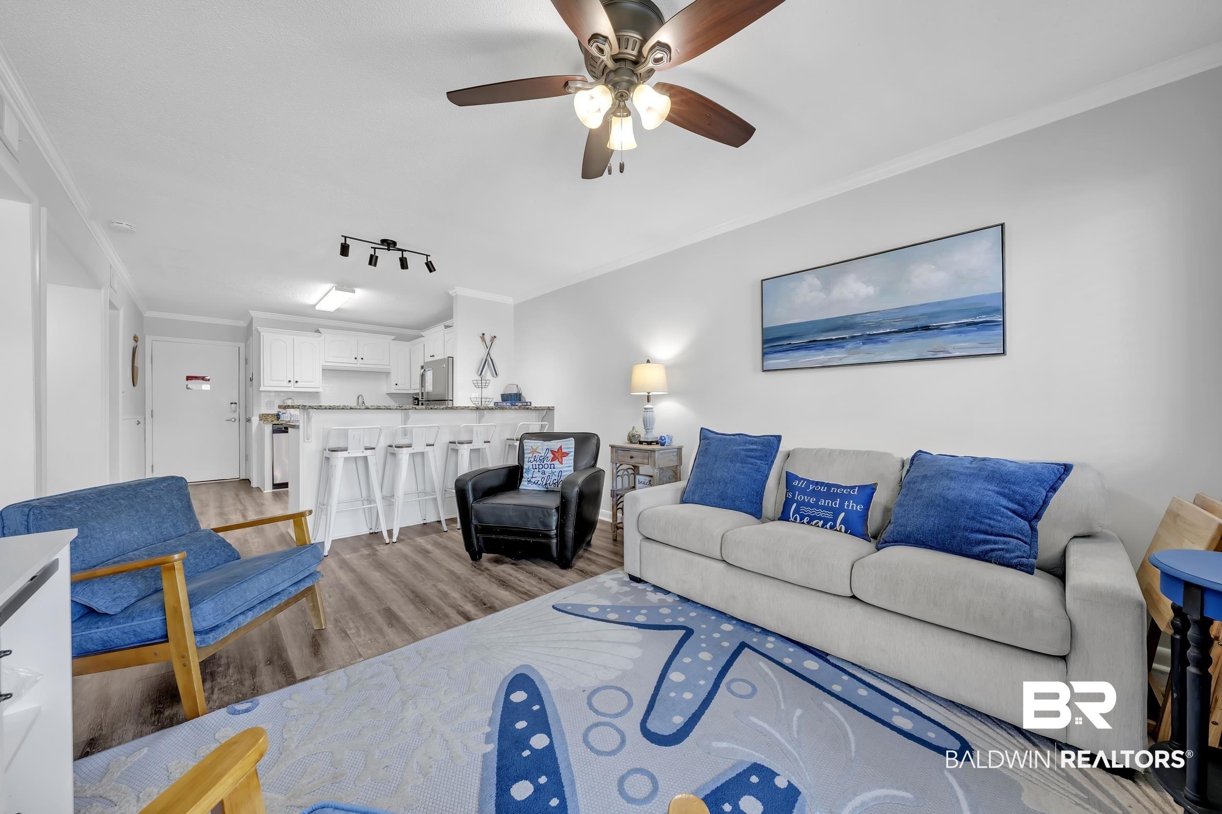 Image 3: Open-concept living area featuring wood-finish flooring, a ceiling fan with integrated lighting, and crown molding